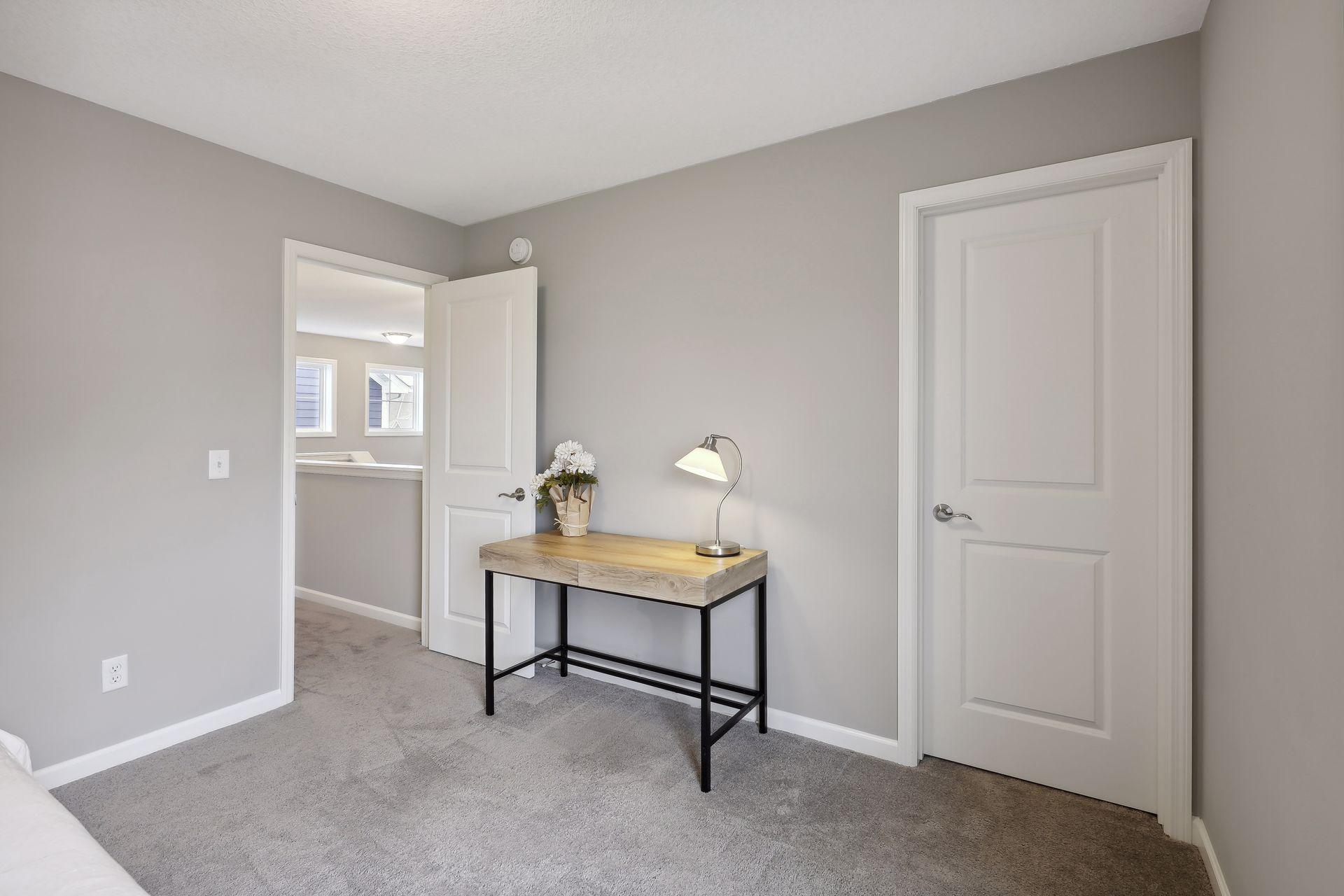 Bedroom with gray carpet and walls, a wood-top desk, and an open doorway to an adjoining room.