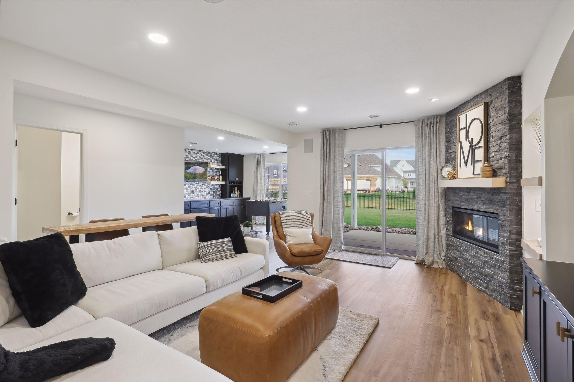 Open-plan living room with a stone fireplace, white sectional, wood floors, and sliding doors to the backyard.