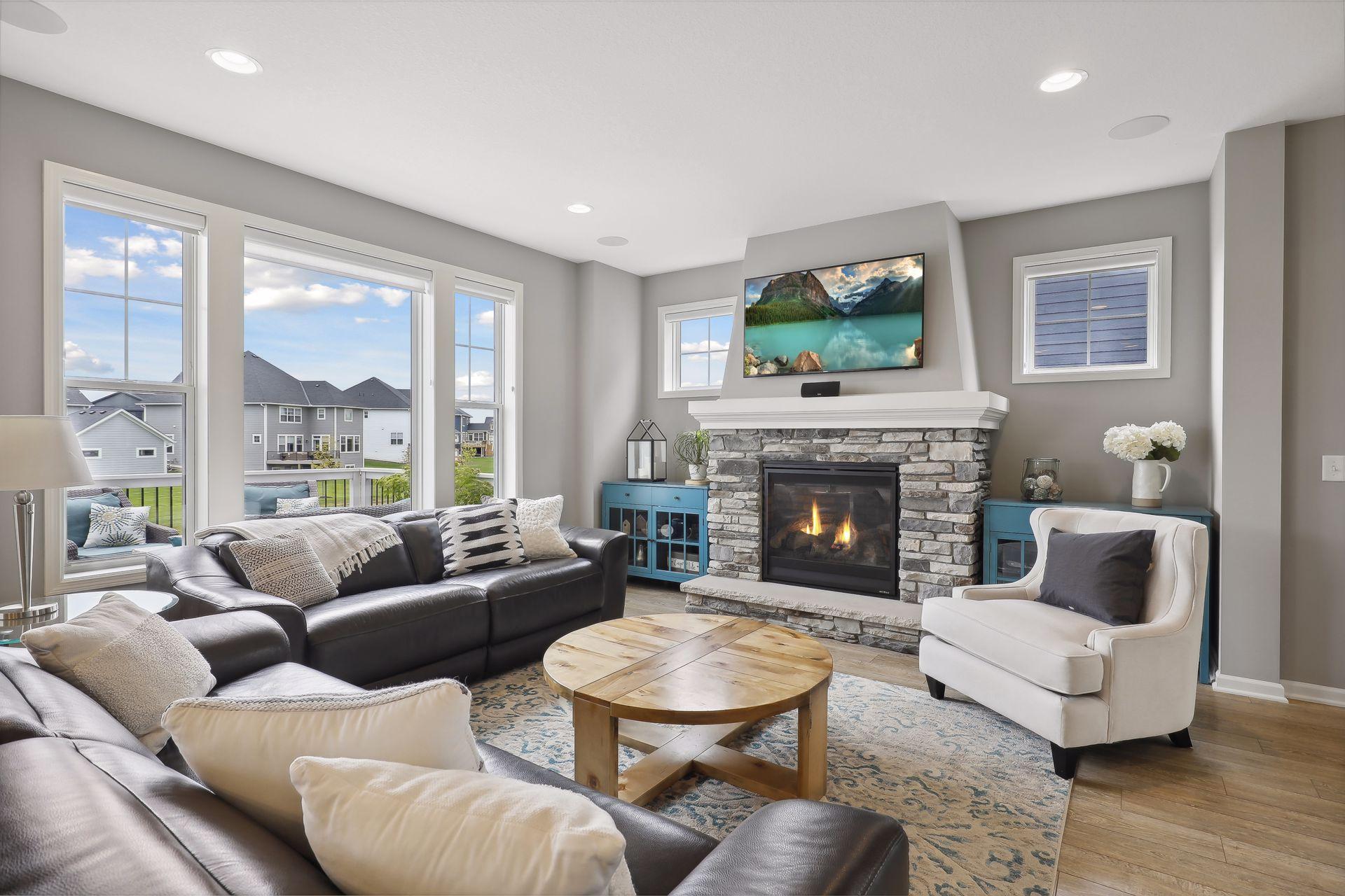 Living room with a stone fireplace, leather sectional, white armchair, and large windows.