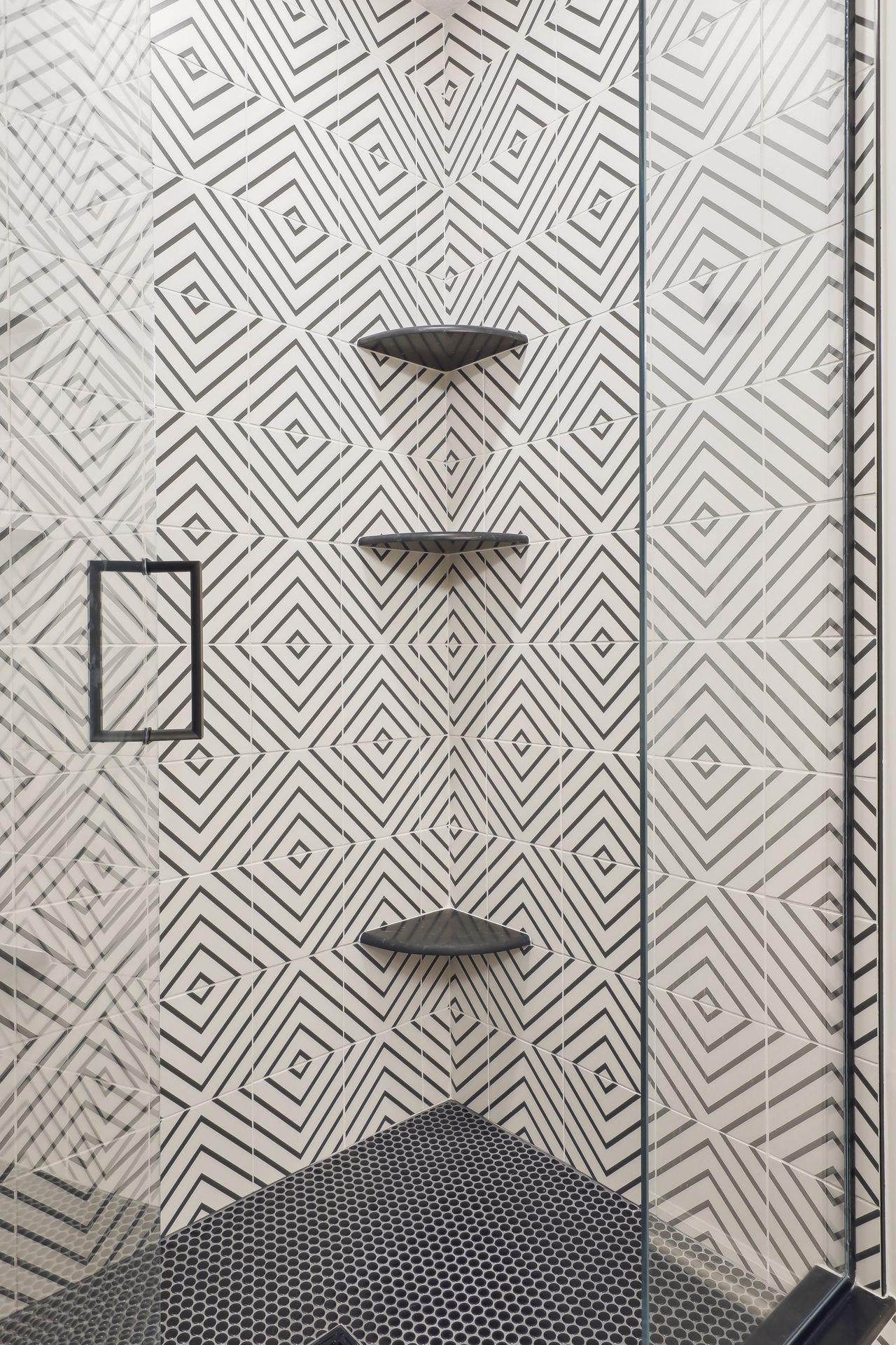 Walk-in shower with geometric black-and-white tile, dark corner shelves, and a pebble-pattern floor.