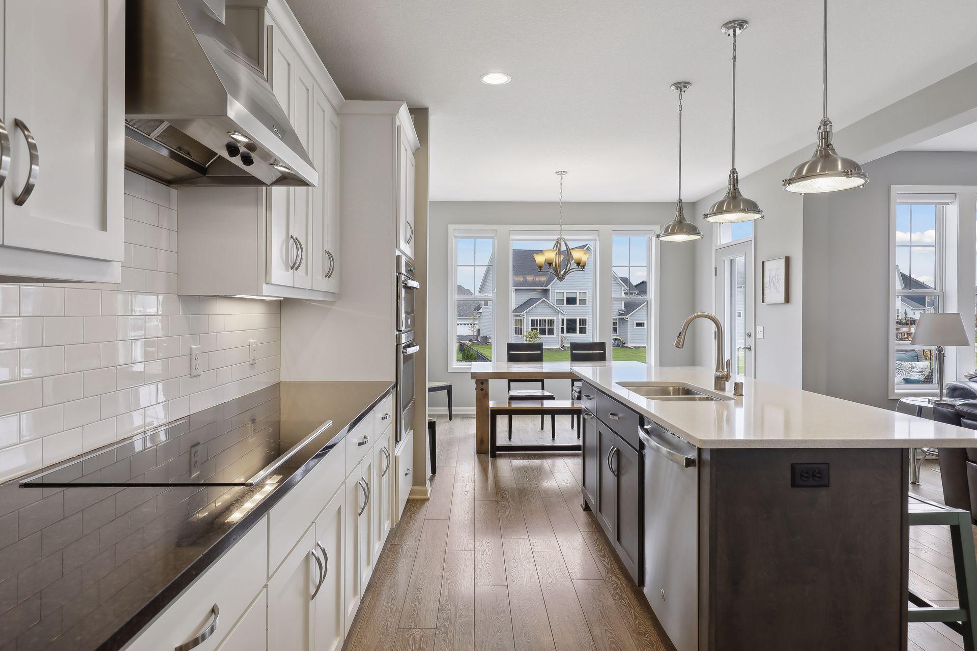 Bright kitchen with white cabinets, tiled backsplash, stainless steel appliances, and a large island beneath pendant lights.