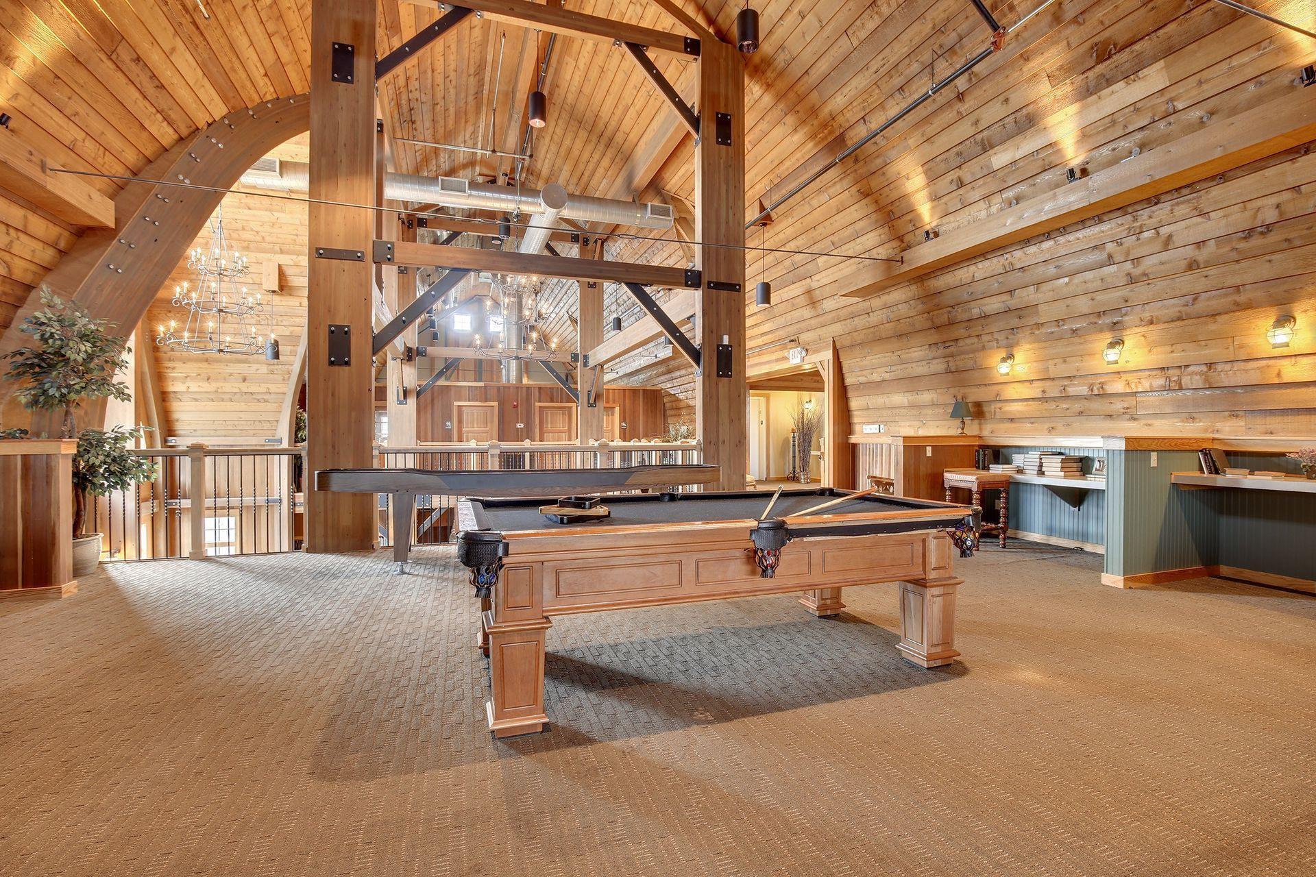 Indoor recreation room with a pool table beneath a vaulted timber ceiling and exposed beams.