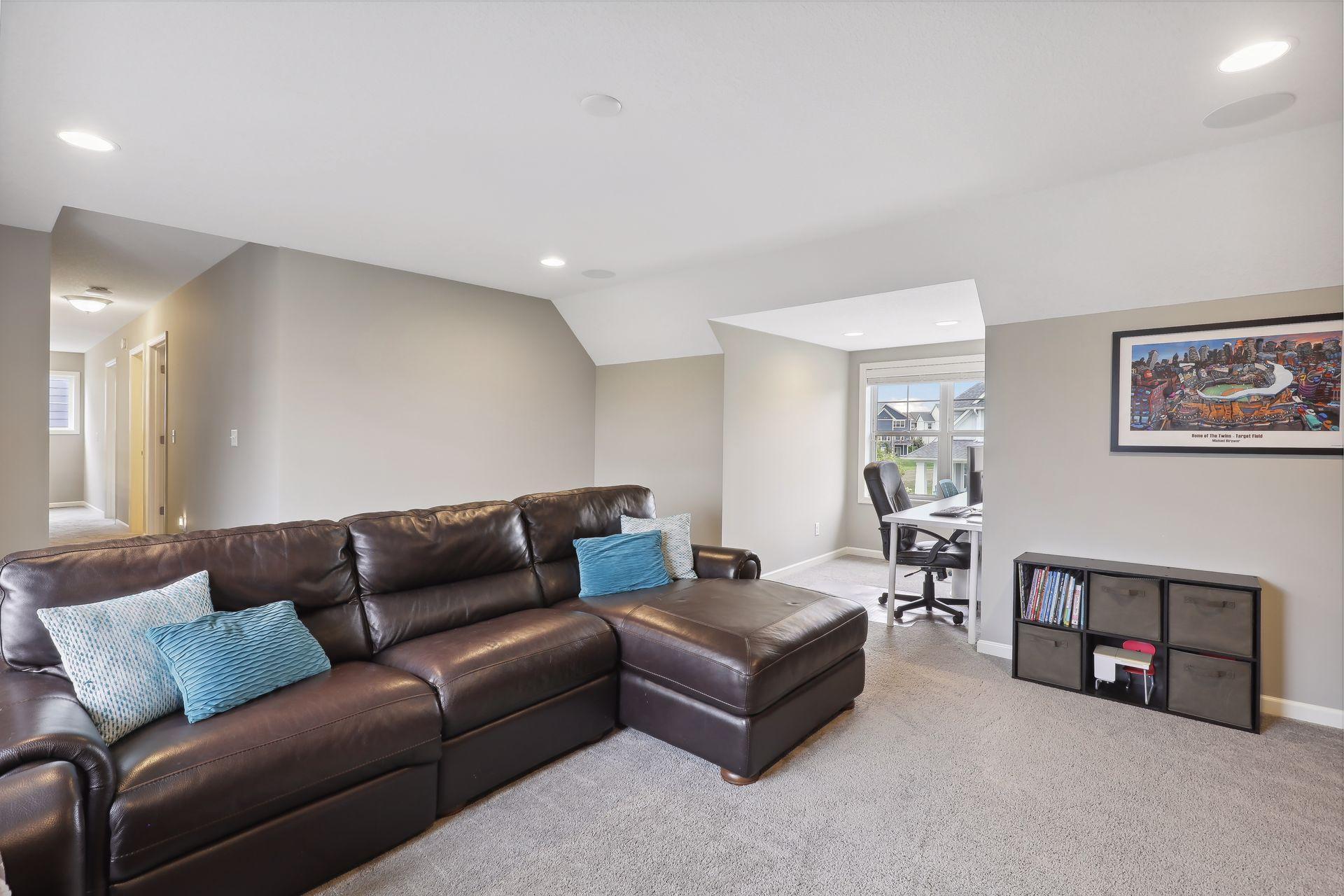 Living room with a brown leather sectional, blue pillows, and an adjoining desk nook.