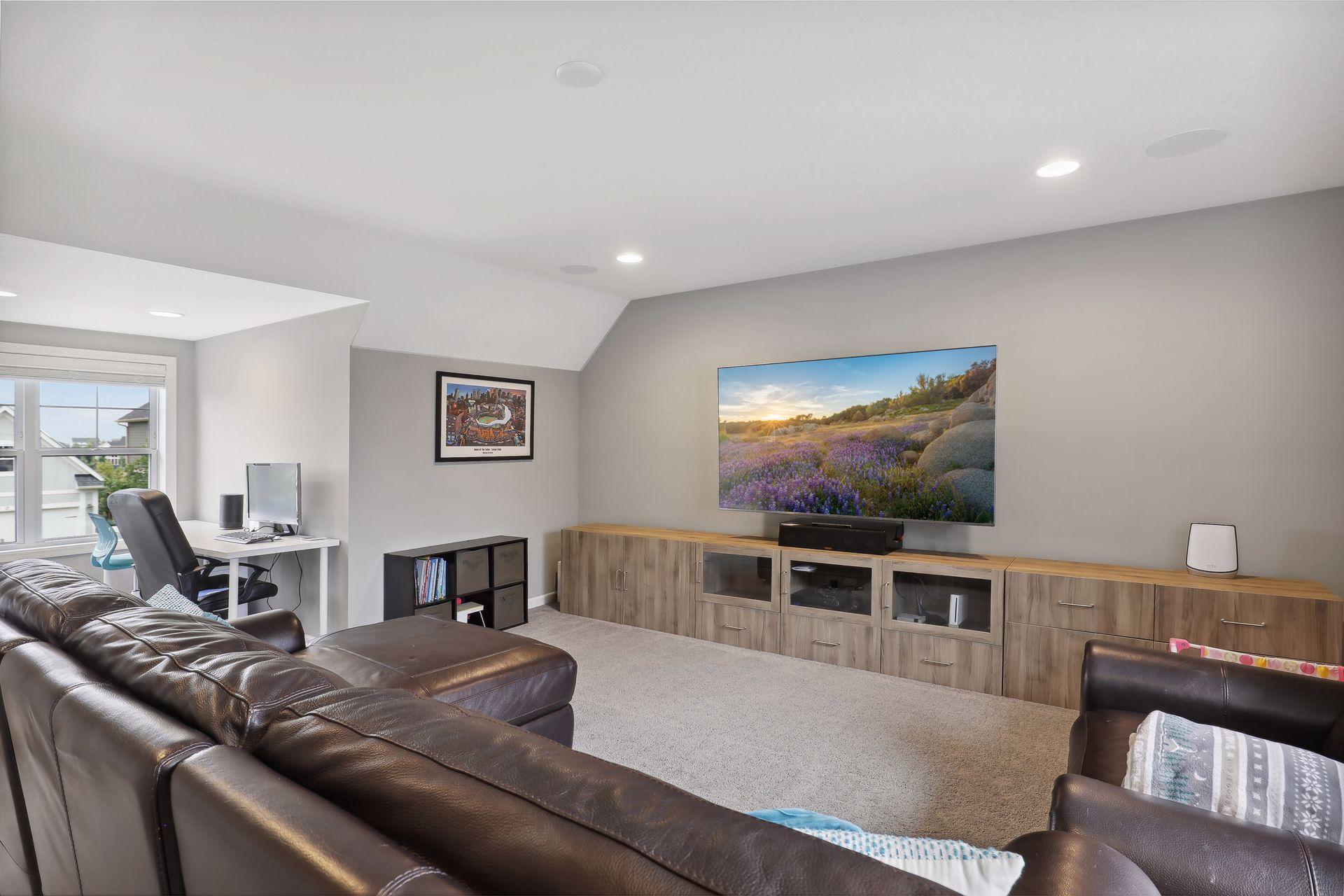 Furnished family room with a leather sectional, large television, and wood media console.
