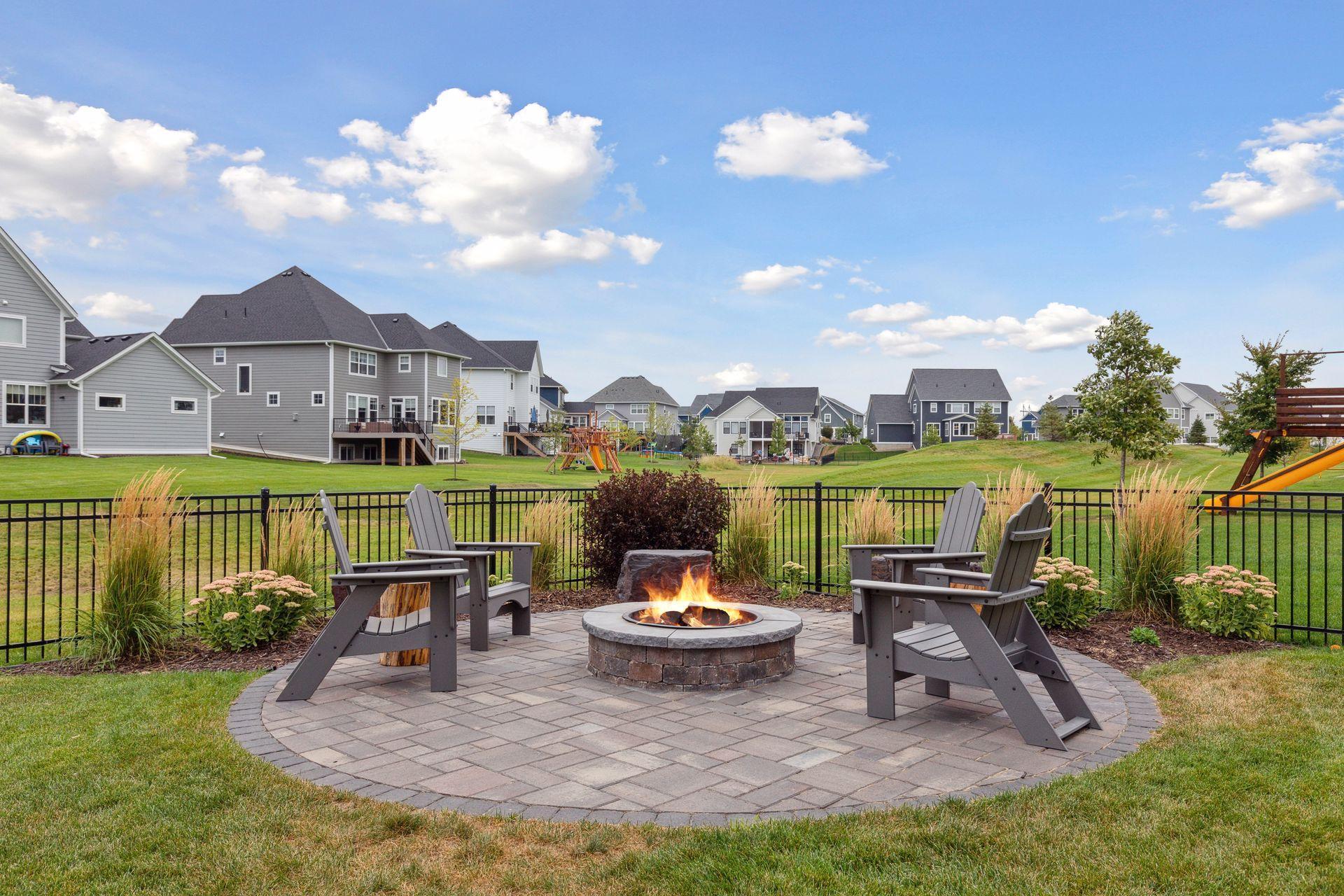 Patio with a stone fire pit and Adirondack chairs overlooking a lawn and neighborhood homes.