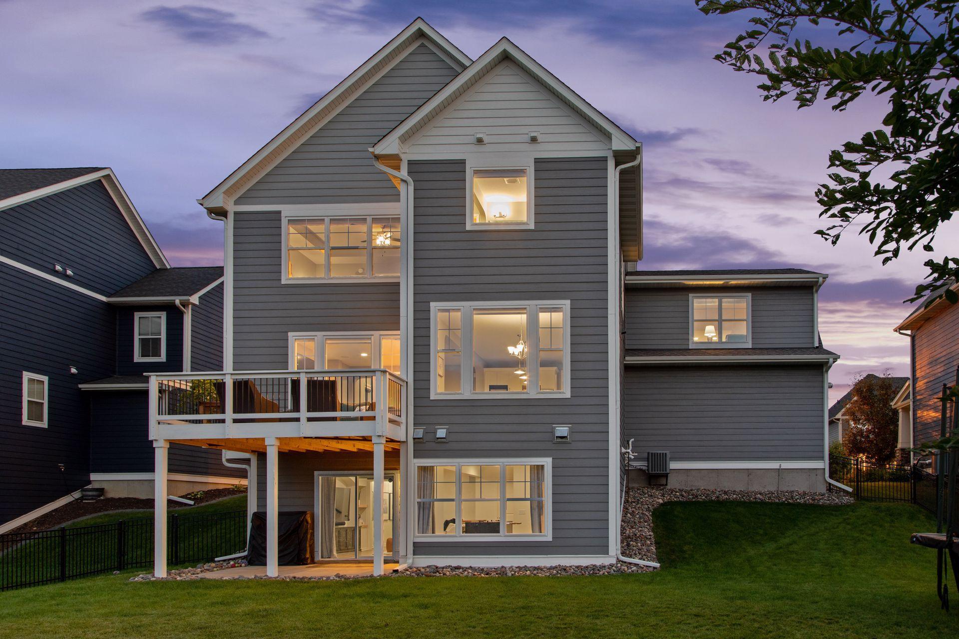 Gray two-story home at dusk with a raised deck and warmly lit windows.