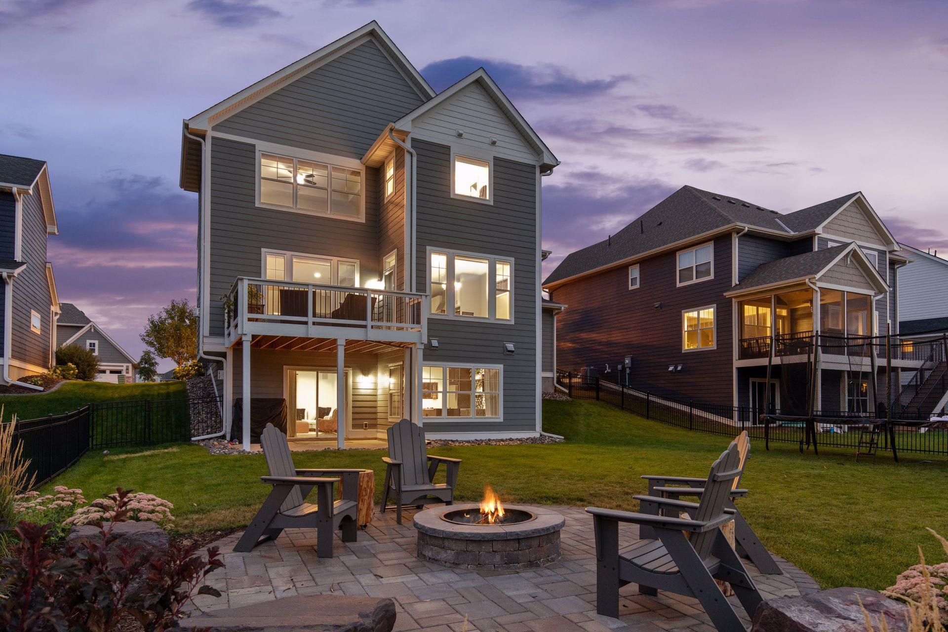 Gray home’s backyard at dusk, with a raised deck and patio seating around a fire pit.