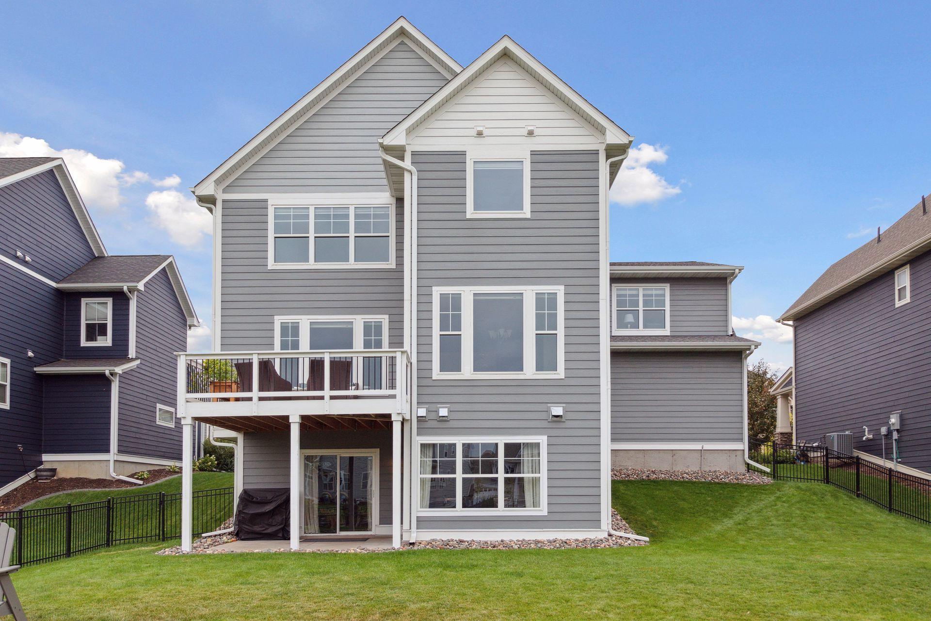 Rear of a gray two-story home with a raised deck and fenced lawn.