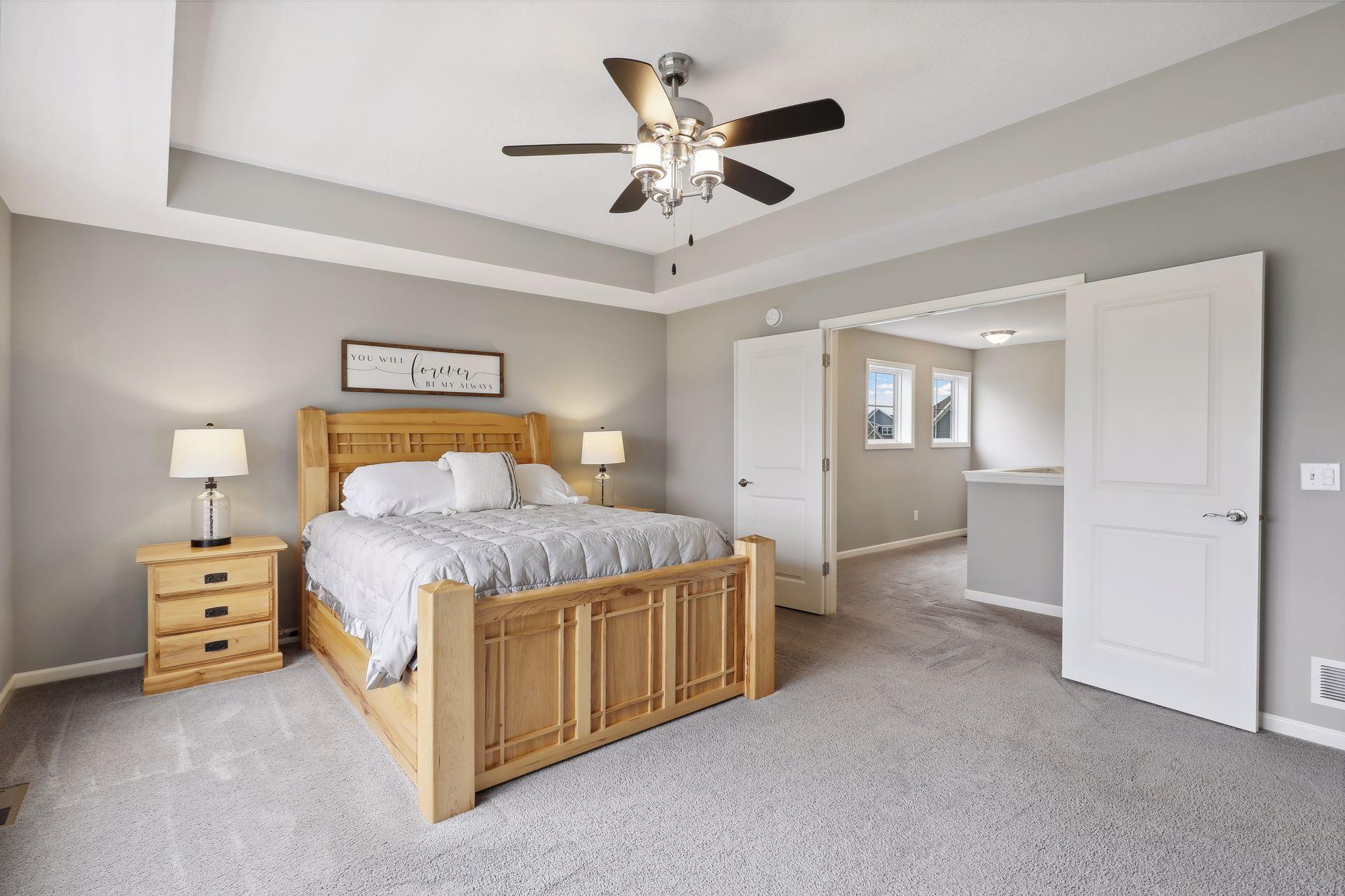 Furnished bedroom with a light-wood bed, white bedding, and tray ceiling with ceiling fan.