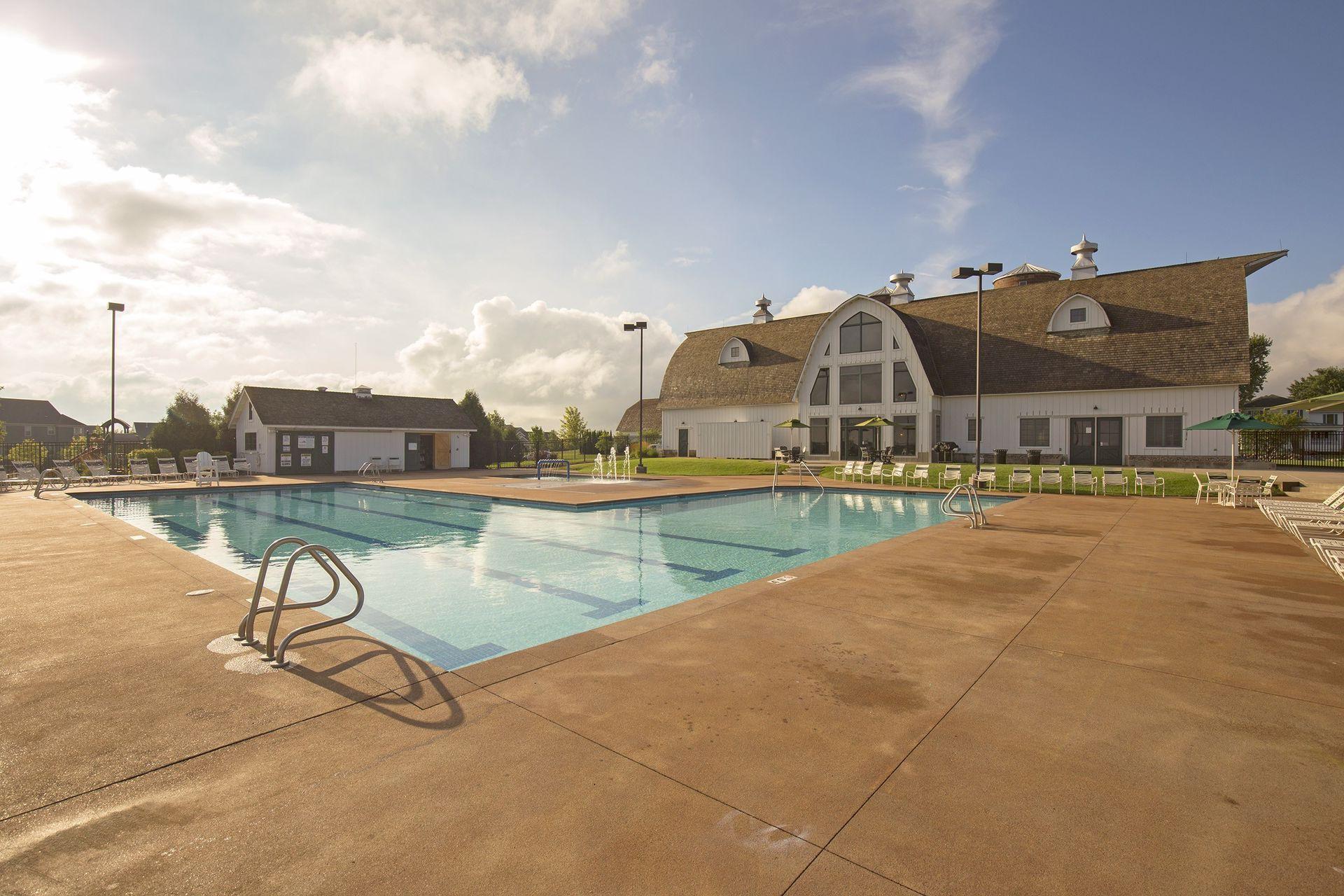 Outdoor pool and deck in front of a large white barn-style clubhouse.