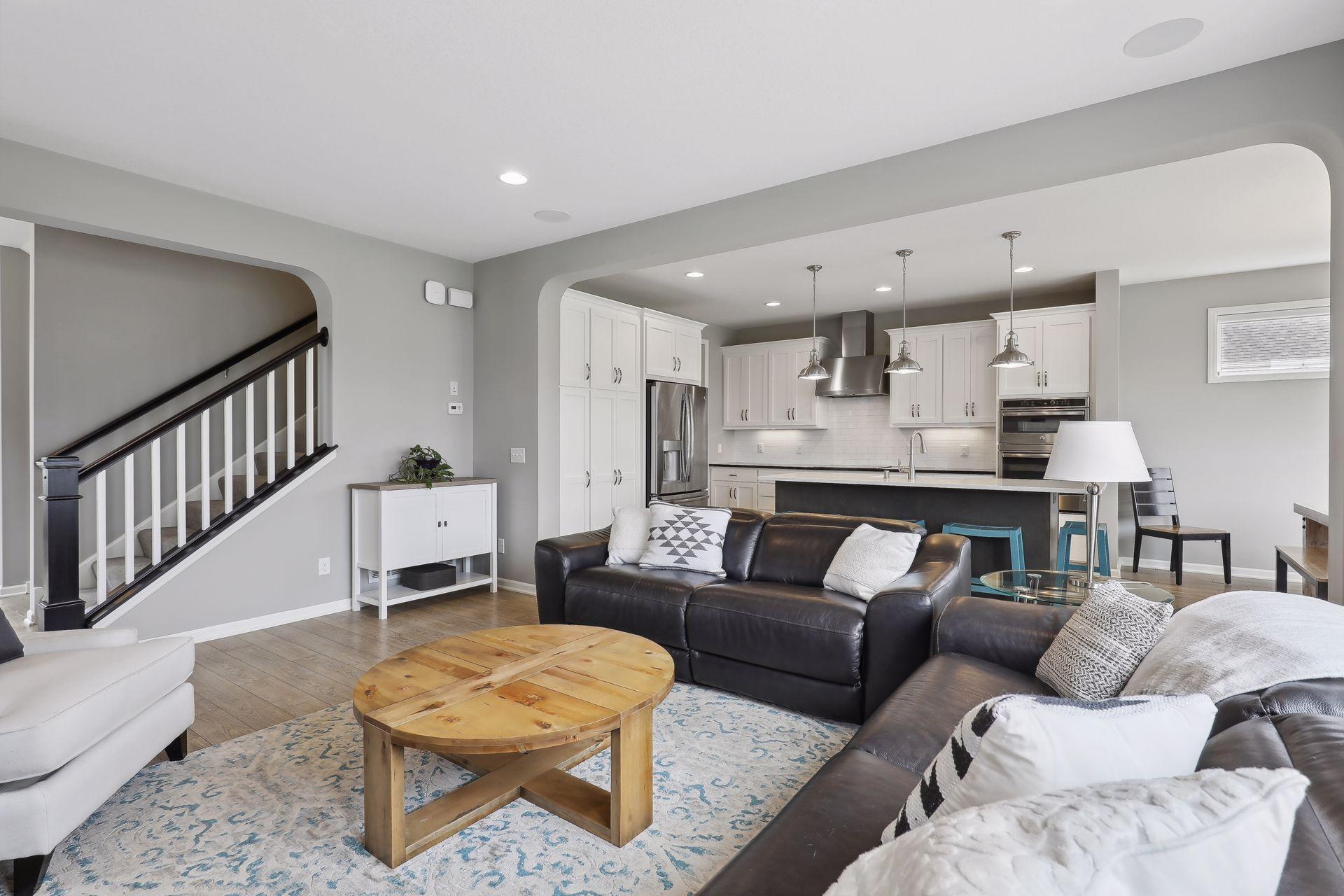 Open-plan living room and kitchen with a dark leather sectional and white cabinetry.