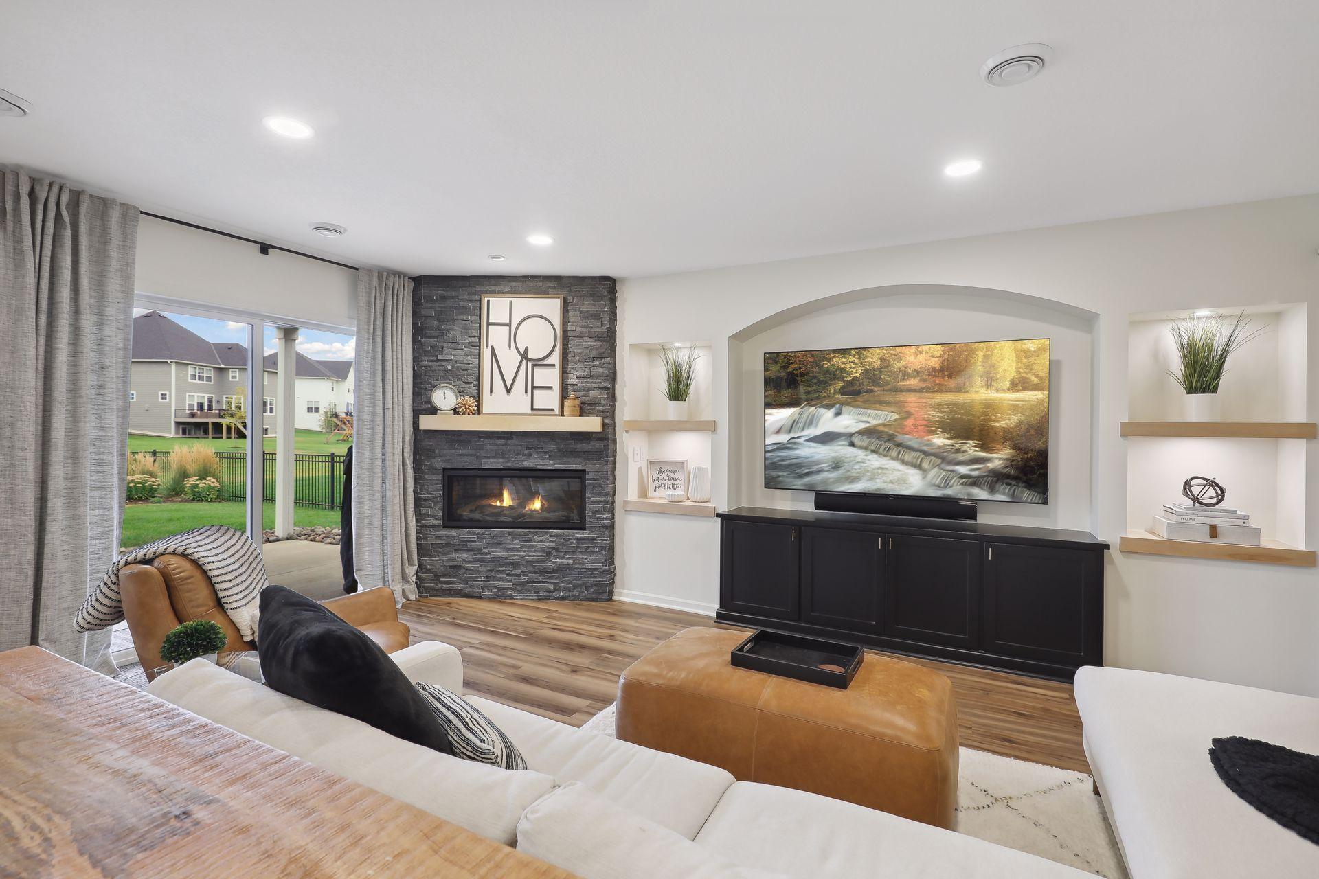 Furnished living room with a stone fireplace, recessed television wall, and sliding doors to the backyard.
