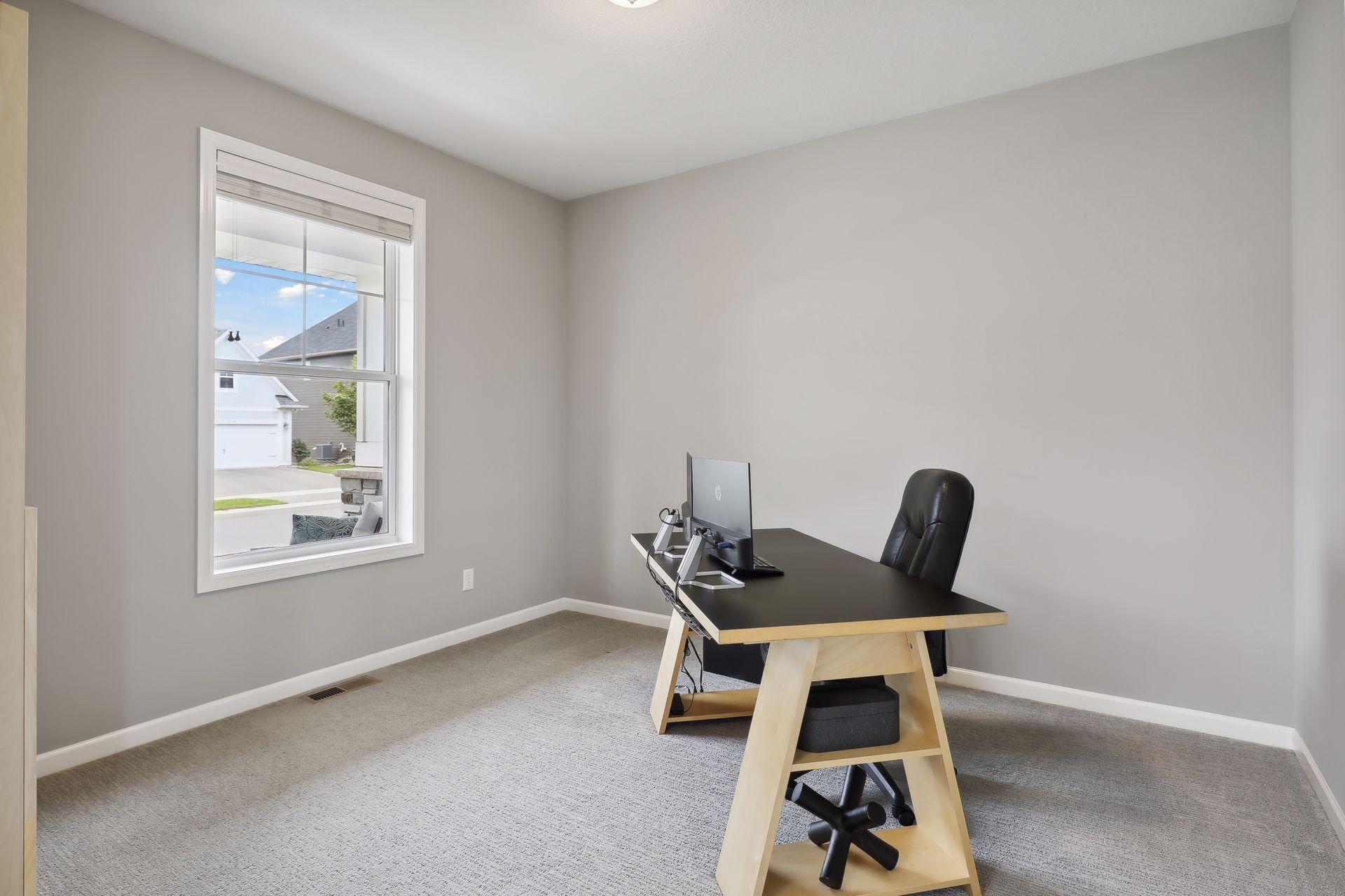 Home office with a black desk and computer beside a window.