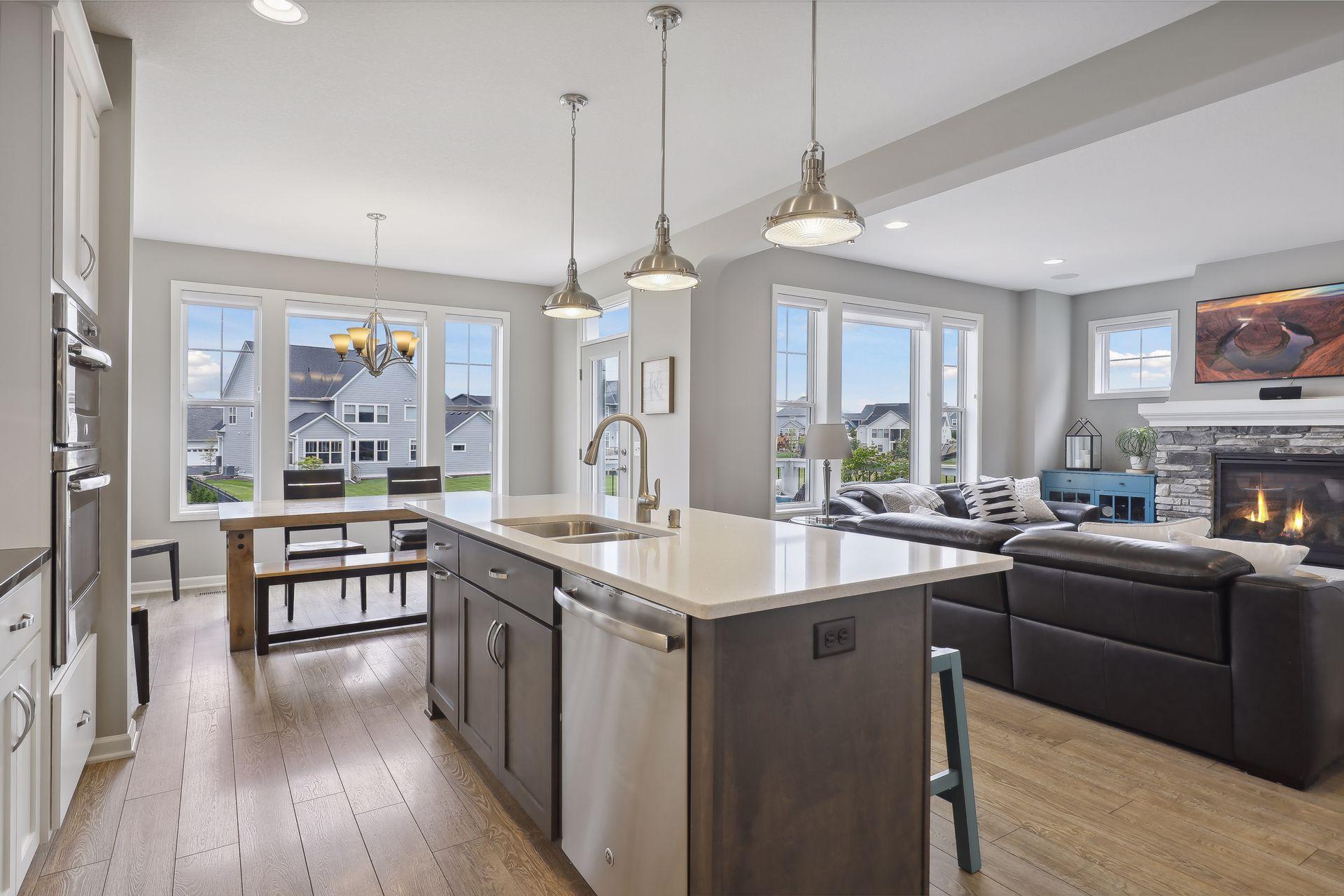 Open kitchen and living room with a large island, stone fireplace, and water visible through the windows.
