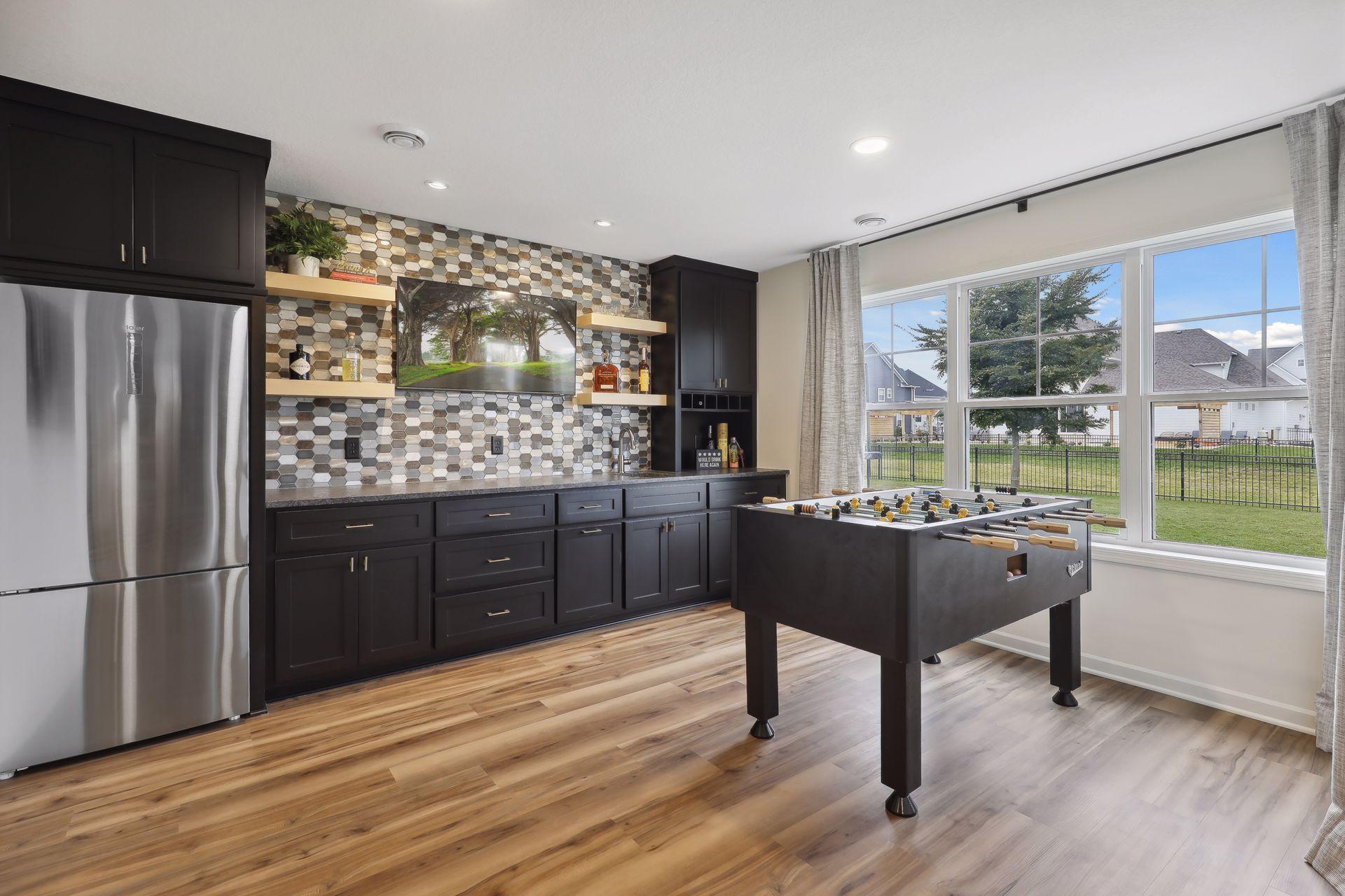 Recreation room with a foosball table, dark built-ins, patterned tile backsplash, and large windows.