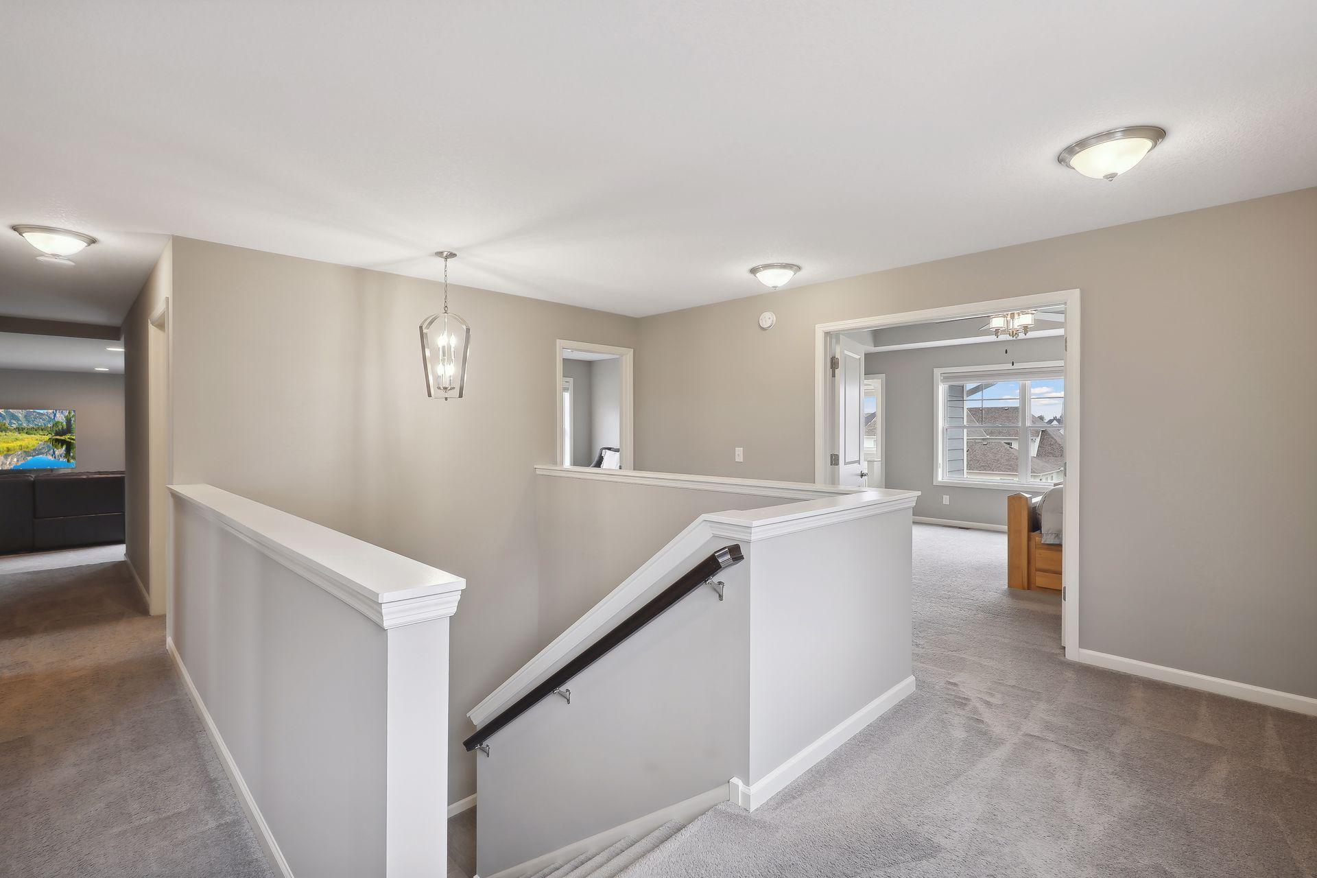 Upstairs landing with carpeted stairs, a dark handrail, and open doorways to bright rooms.