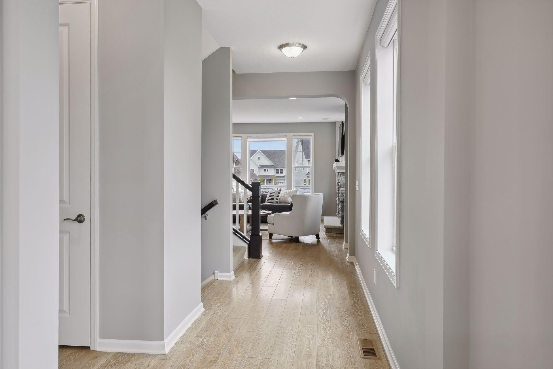 Bright hallway with light wood floors and tall windows opening onto a furnished living room.