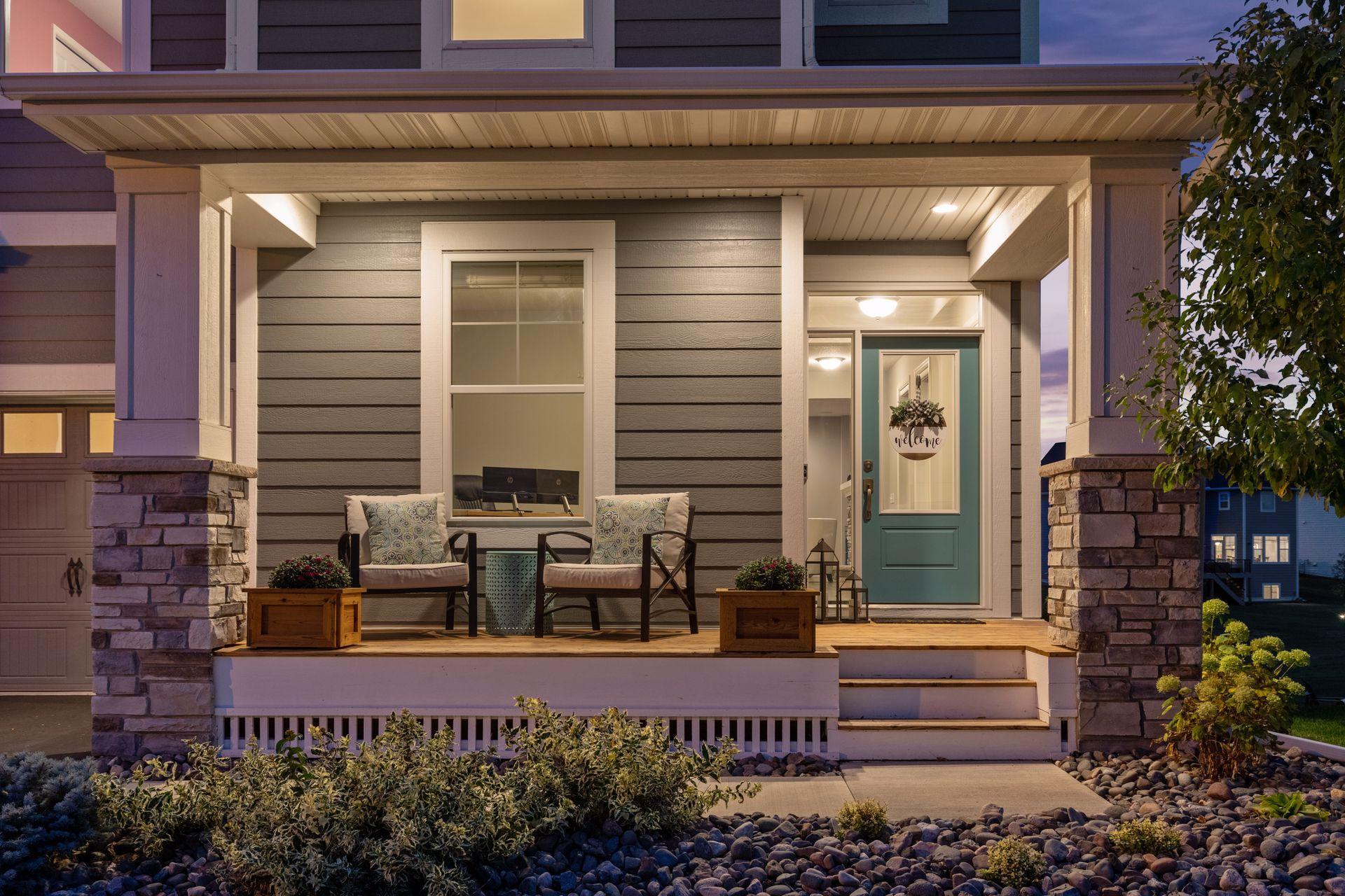 Home exterior at dusk with a covered, furnished porch, stone columns, and a teal front door.