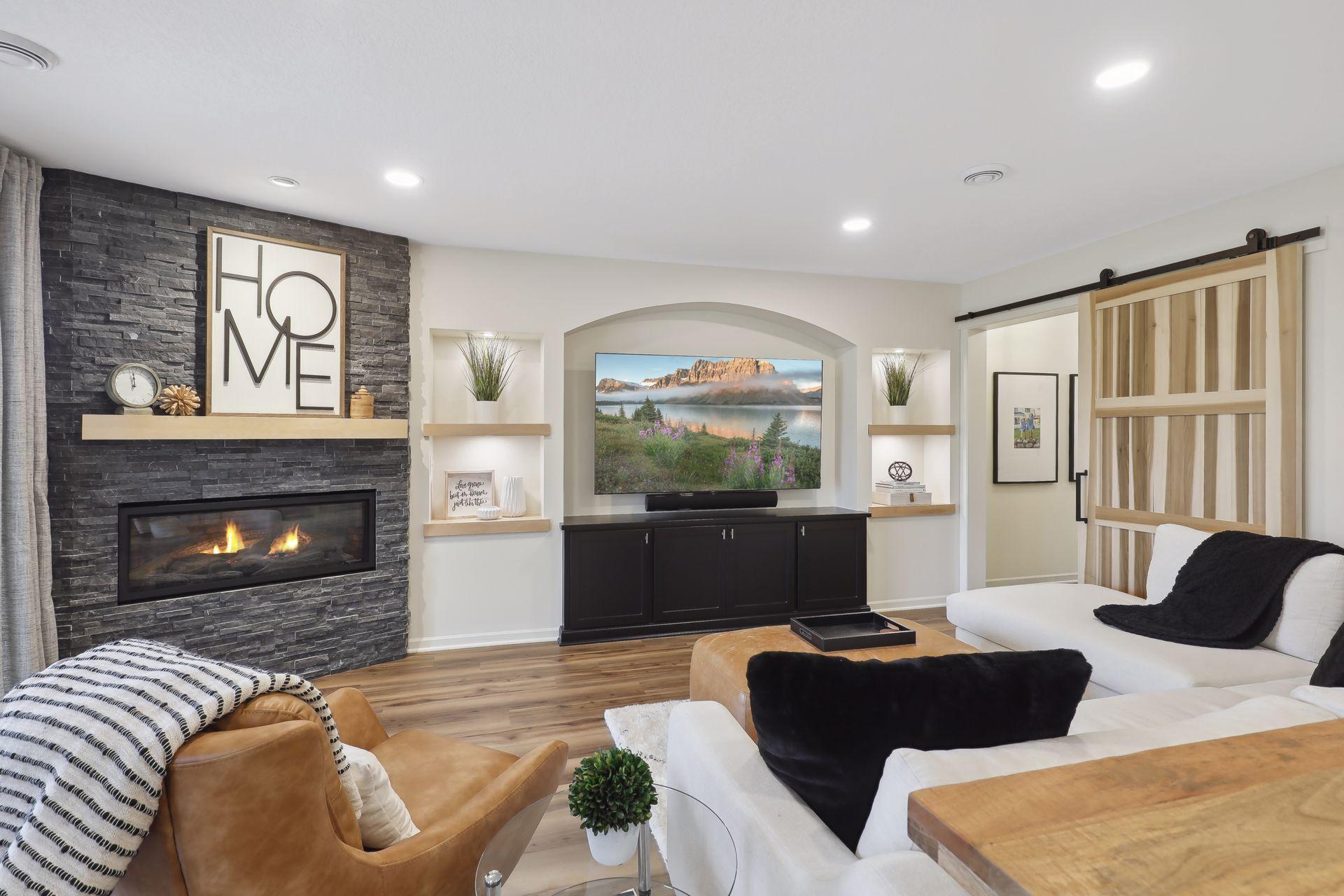 Staged living room with a stone fireplace, television alcove, and sliding wood barn door.