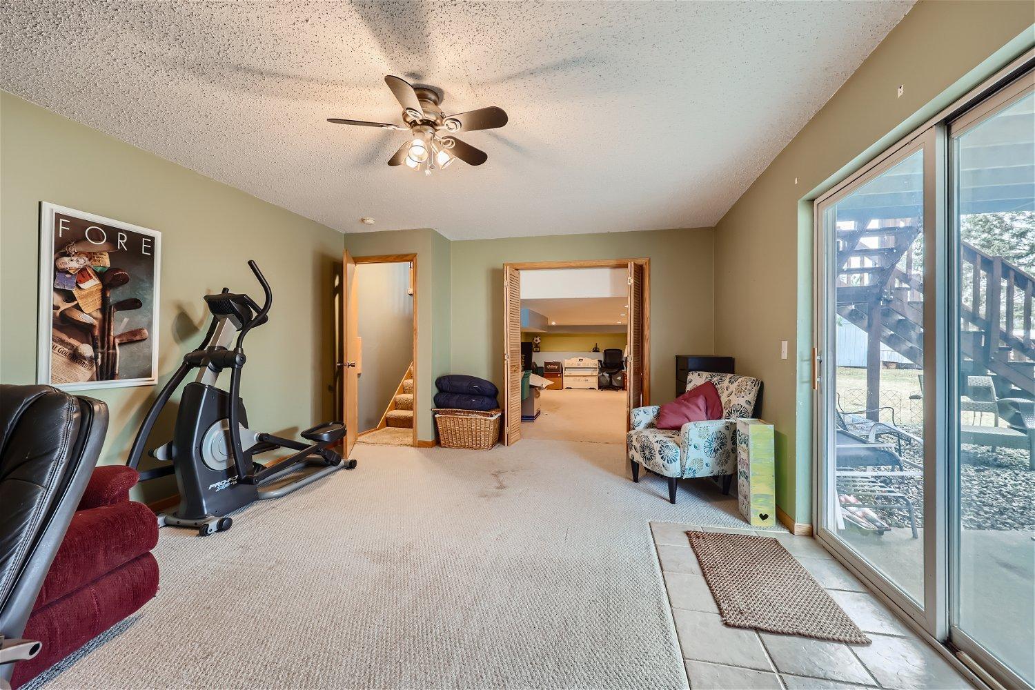 Lower-level living area with an elliptical machine, seating, and sliding glass doors to a deck.