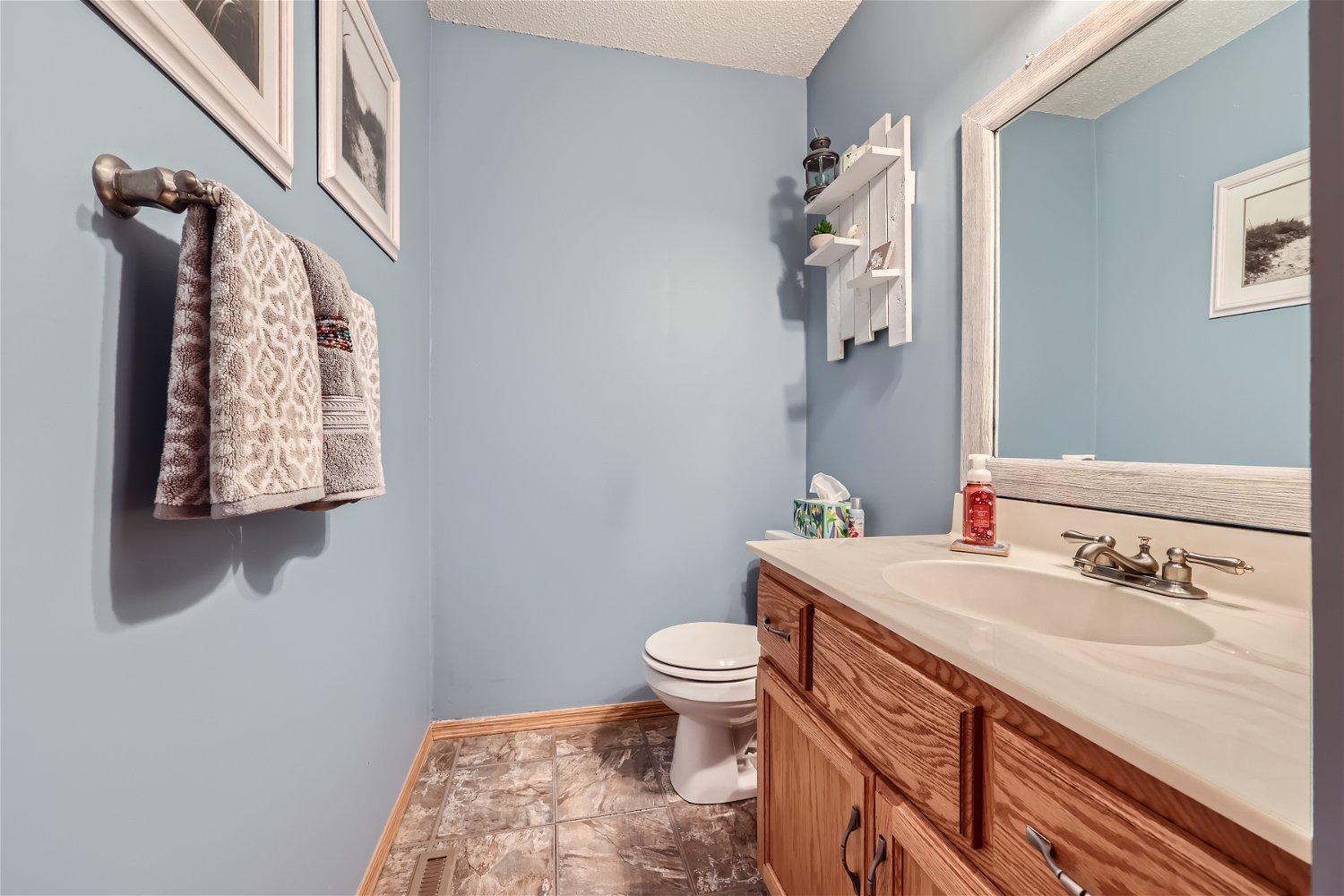Bathroom with a wood vanity, white sink, toilet, and light blue walls.