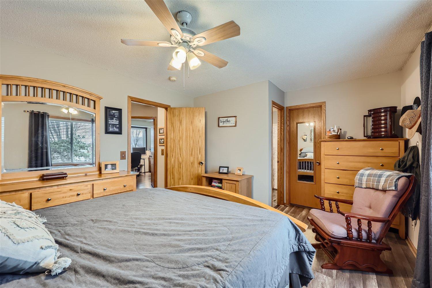 Furnished bedroom with gray bedding, wood furniture, a large vanity mirror, and a ceiling fan.
