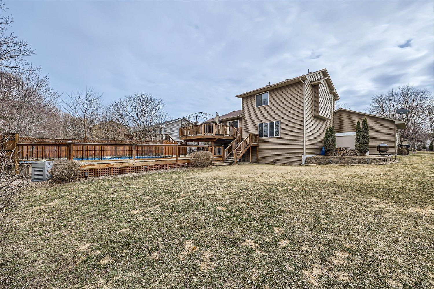 Rear of a tan two-story house with a raised deck, fenced pool, and broad lawn.