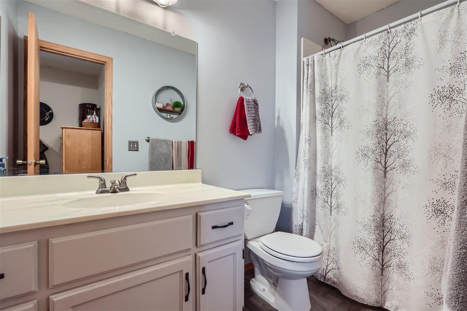 Bathroom with paneled vanity, toilet, and tree-patterned shower curtain.