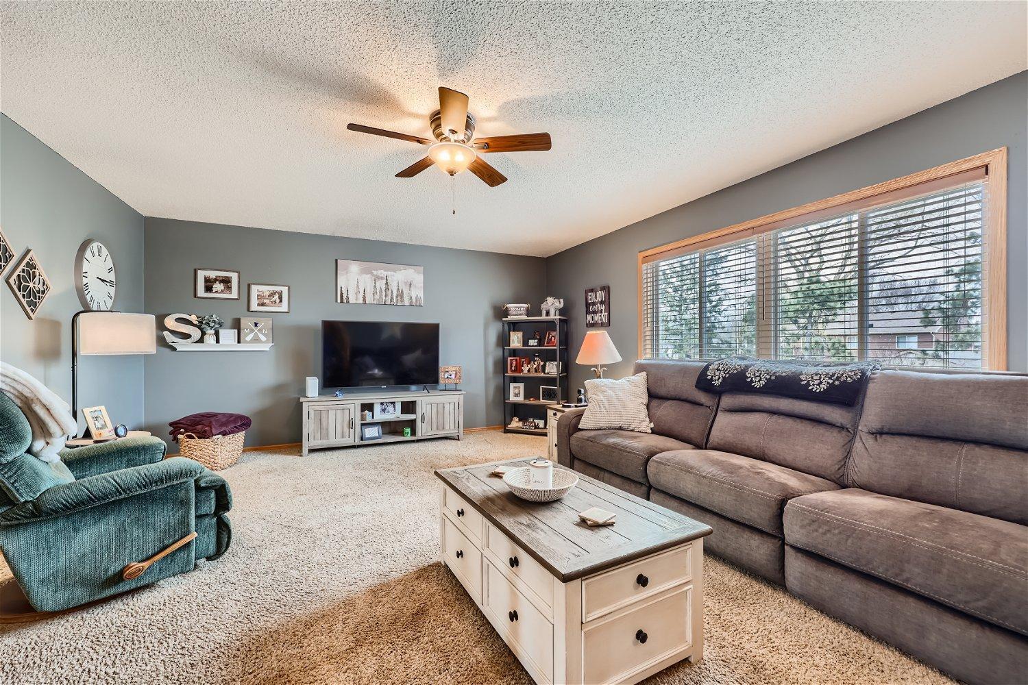 Living room with a gray sectional, teal armchair, and wide windows with blinds.
