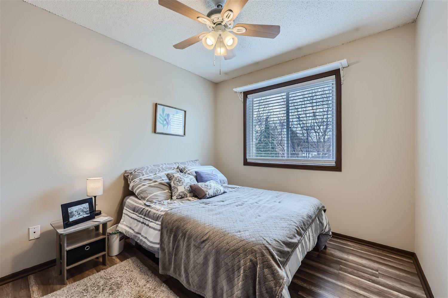 Furnished bedroom with gray bedding, a ceiling fan, and a large window overlooking snowy trees.
