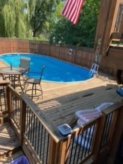 Backyard pool beside a spacious wooden deck with patio furniture and an American flag.
