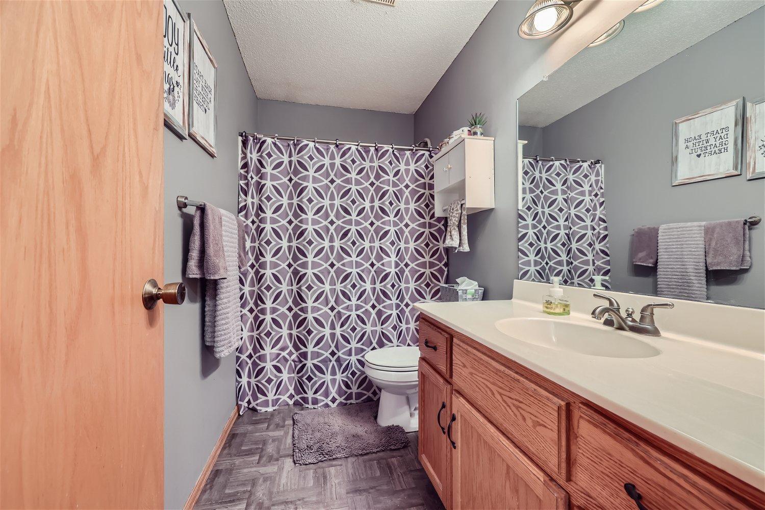 Bathroom with a long wood vanity, large mirror, and purple-and-white patterned shower curtain.