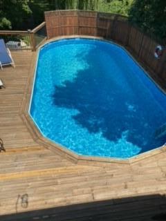 Backyard swimming pool surrounded by a wooden deck and privacy fence.