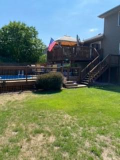 House backyard with a raised wooden deck, exterior stairs, fenced pool, and lawn.