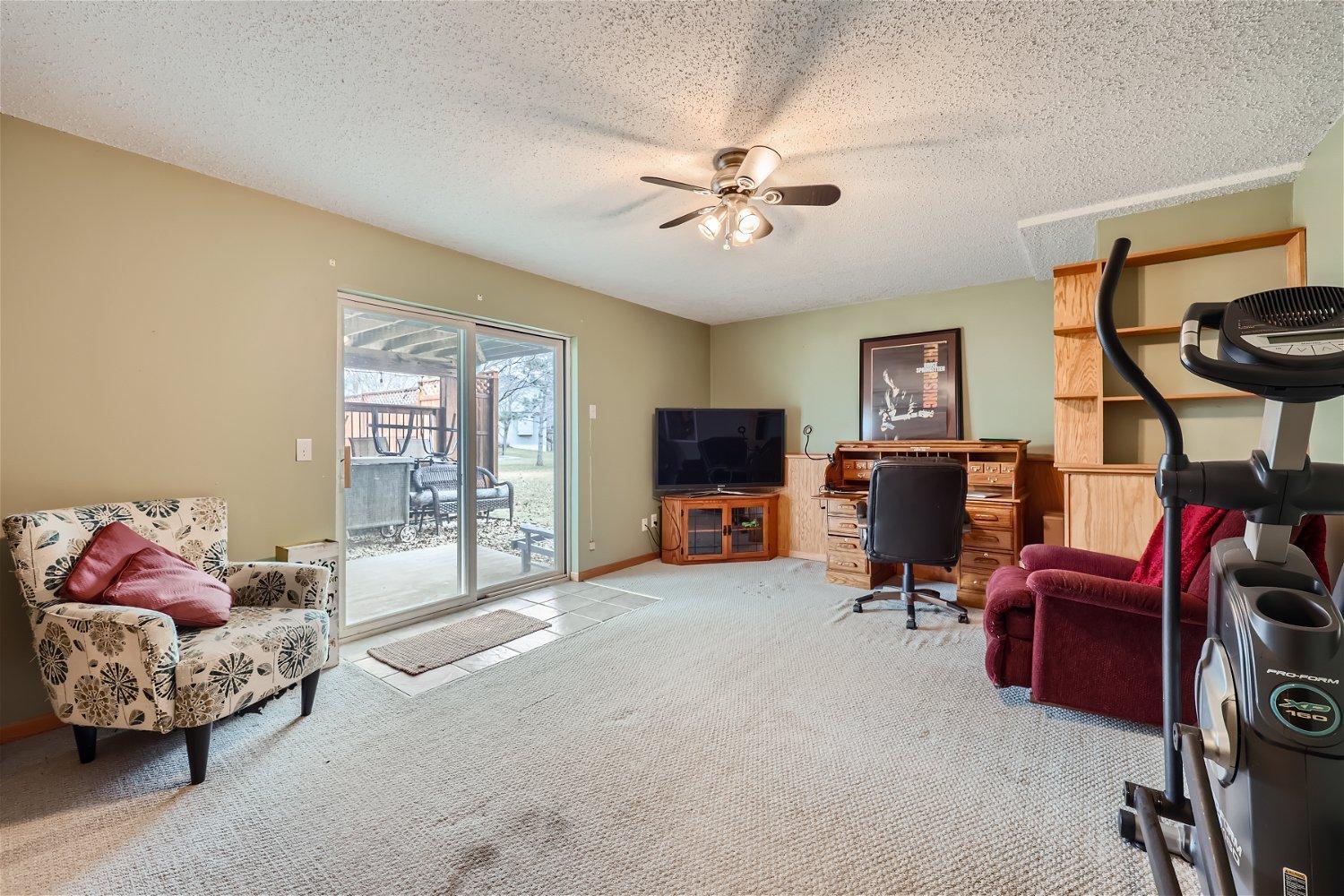 Furnished room with a desk, elliptical trainer, patterned armchair, and sliding doors to a patio.