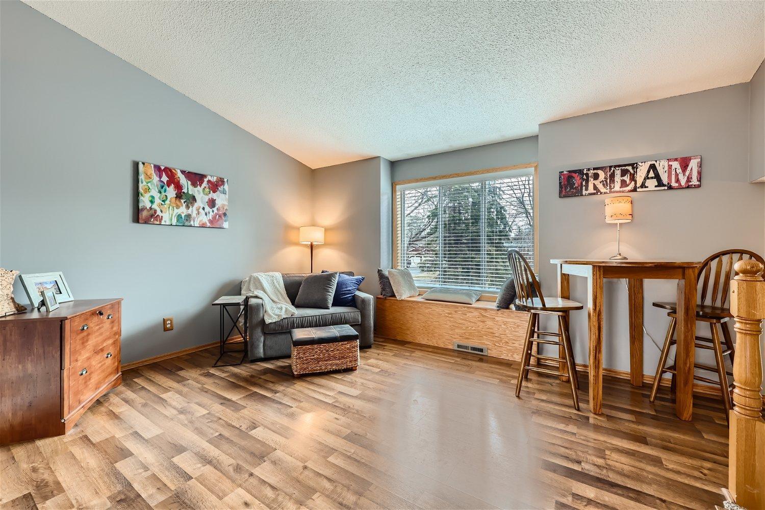 Living and dining area with a gray loveseat, window seat, and wood-look flooring.