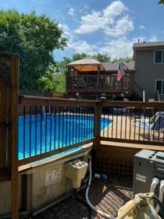 Backyard swimming pool enclosed by a fence, beside a raised deck with an orange canopy.