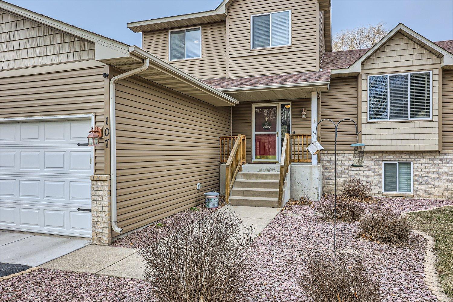Two-story tan-sided home with a white double garage and red front door.