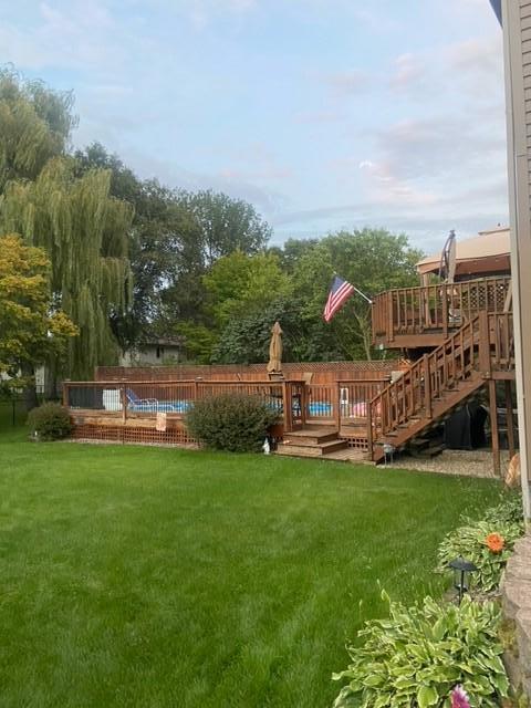 Backyard swimming pool surrounded by wooden decks, stairs, lawn, and mature trees.
