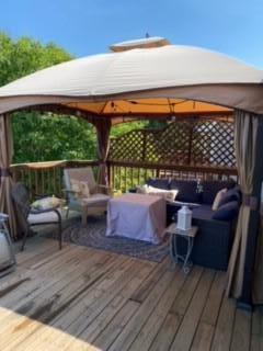 Covered patio with cushioned seating beneath a gazebo on a wooden deck.