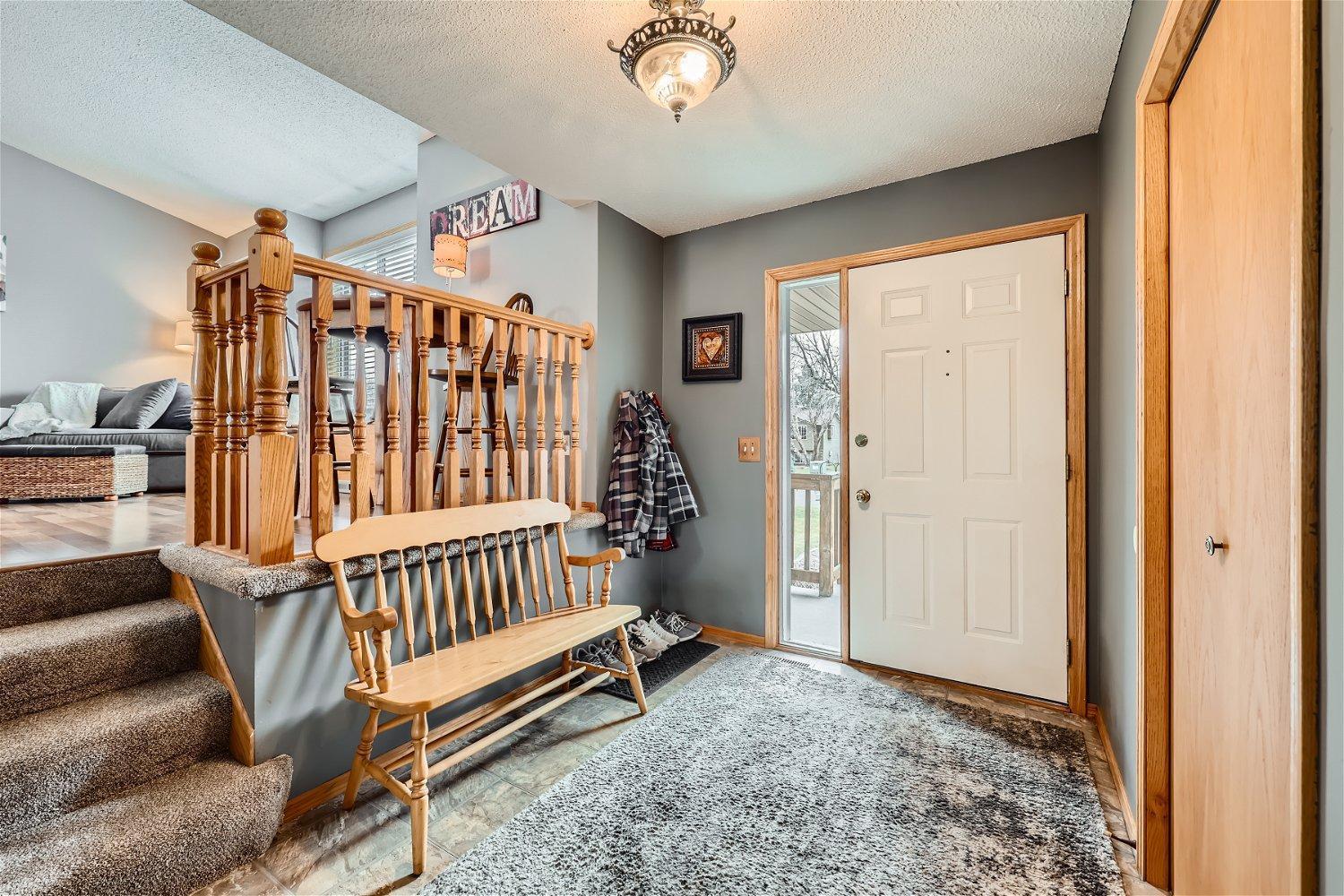Home entryway with a white front door, wooden bench, and carpeted stairs beside the living room.