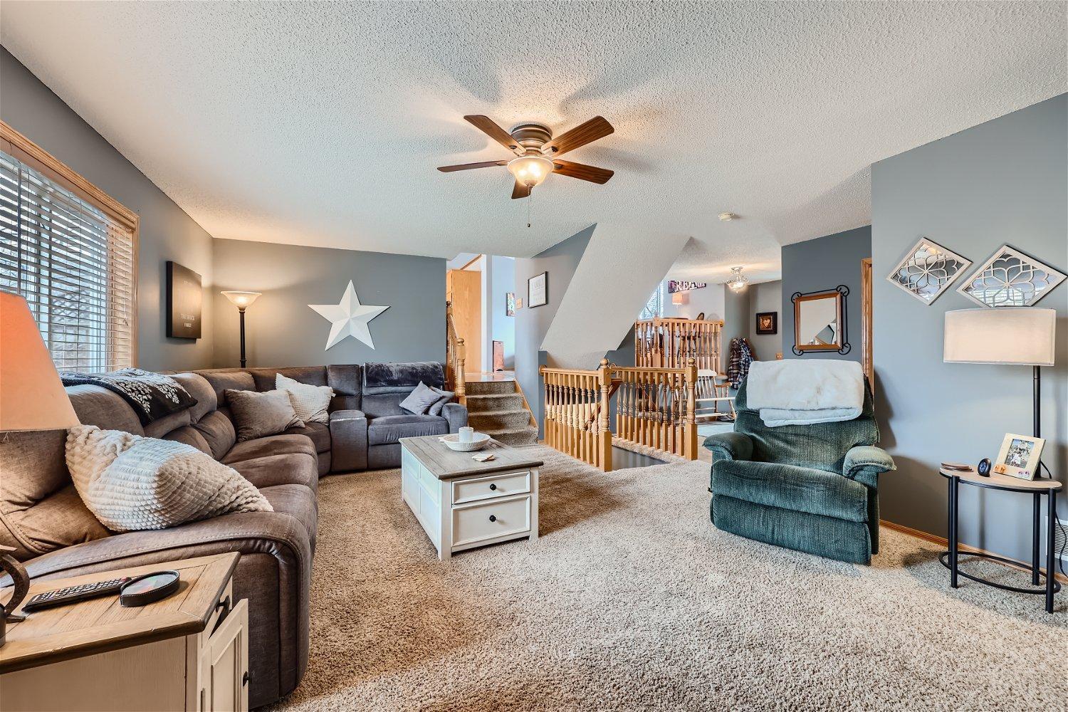 Furnished living room with a gray sectional, green recliner, and carpeted stairs with wood railing.