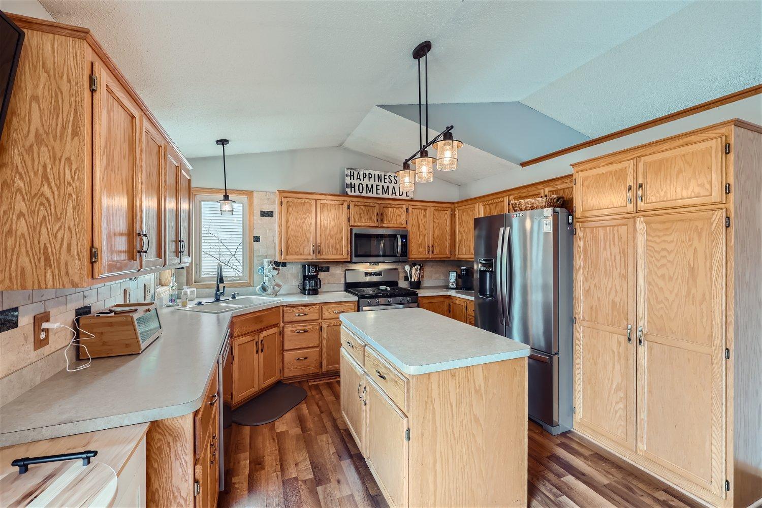 Kitchen with oak cabinetry, a central island, stainless steel appliances, and pendant lighting.