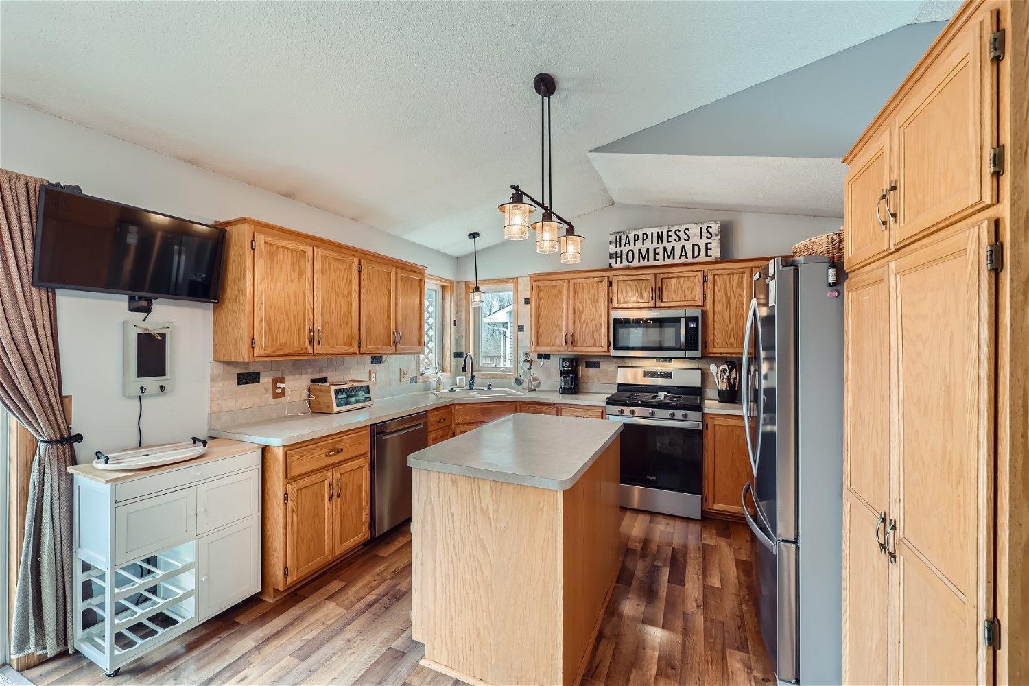 Kitchen with honey-colored wood cabinets, a central island, stainless steel appliances, and hardwood flooring.