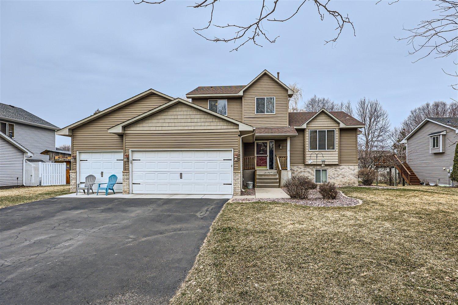 Two-story tan house with a stone-accented facade, three-car garage, and wide driveway.