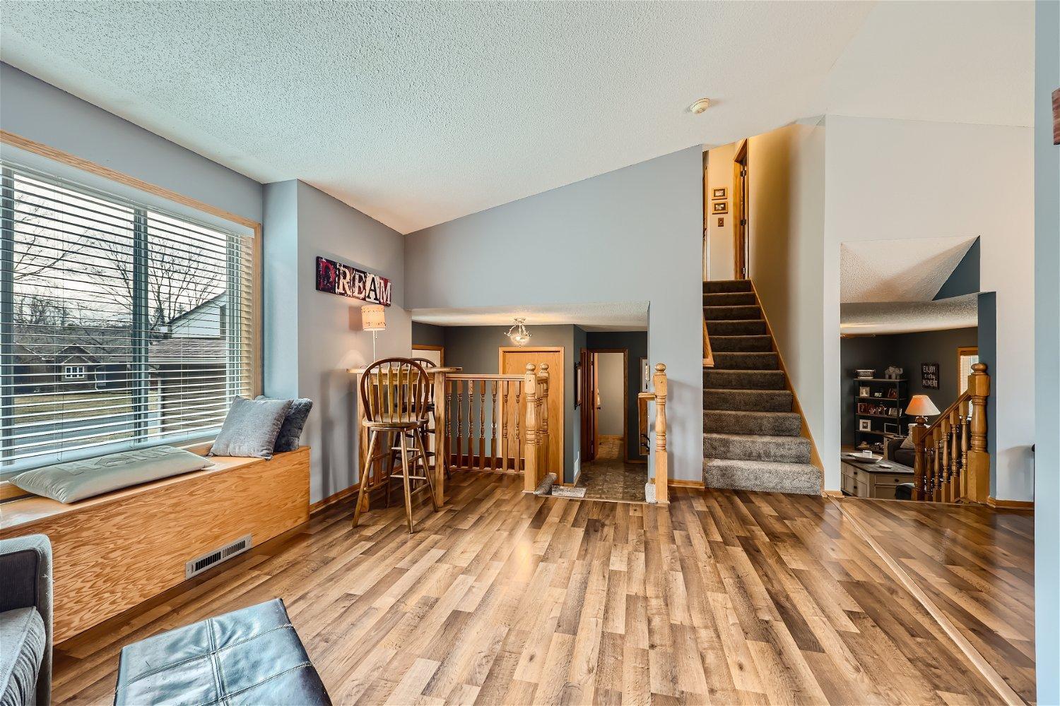 Living area with wood-look flooring, a window bench, and an open staircase.
