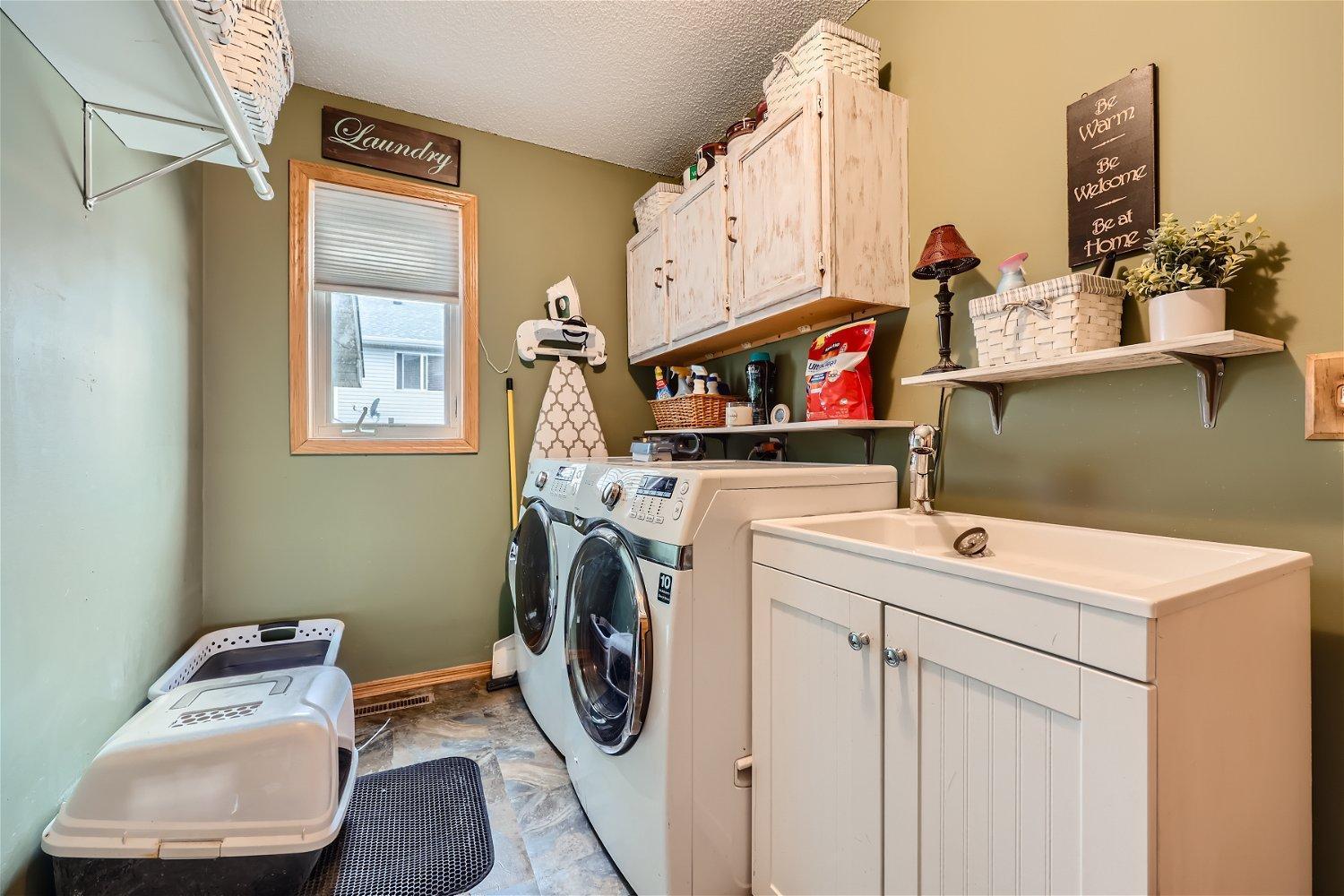 Laundry room with front-loading washer and dryer, utility sink, and whitewashed cabinets.