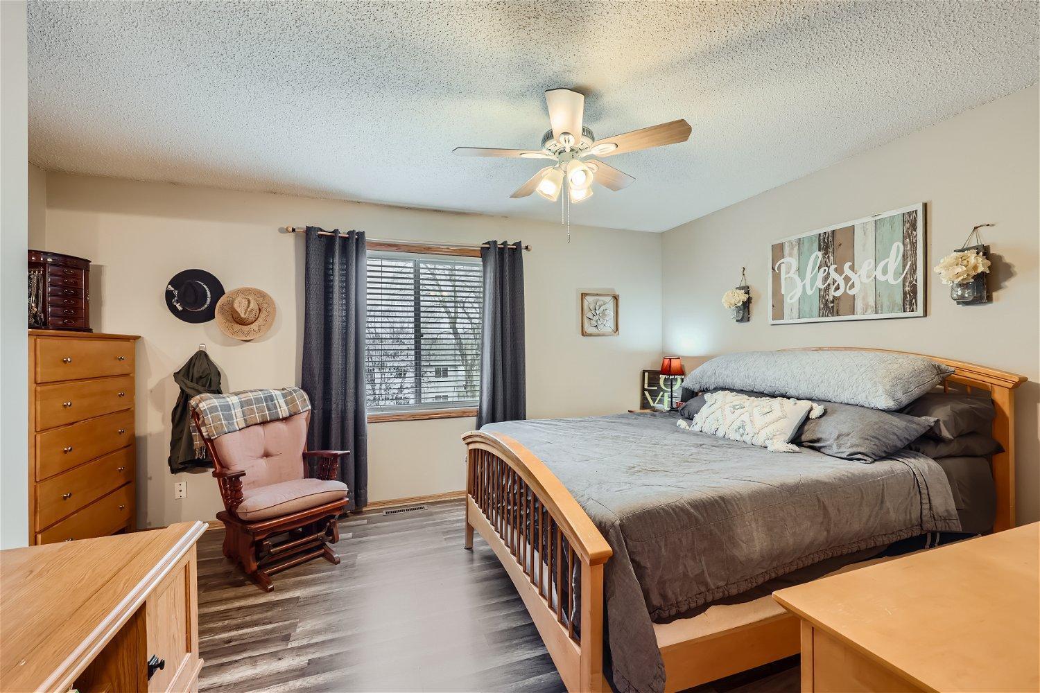 Furnished bedroom with a wooden bed, gray bedding, ceiling fan, and rocking chair.