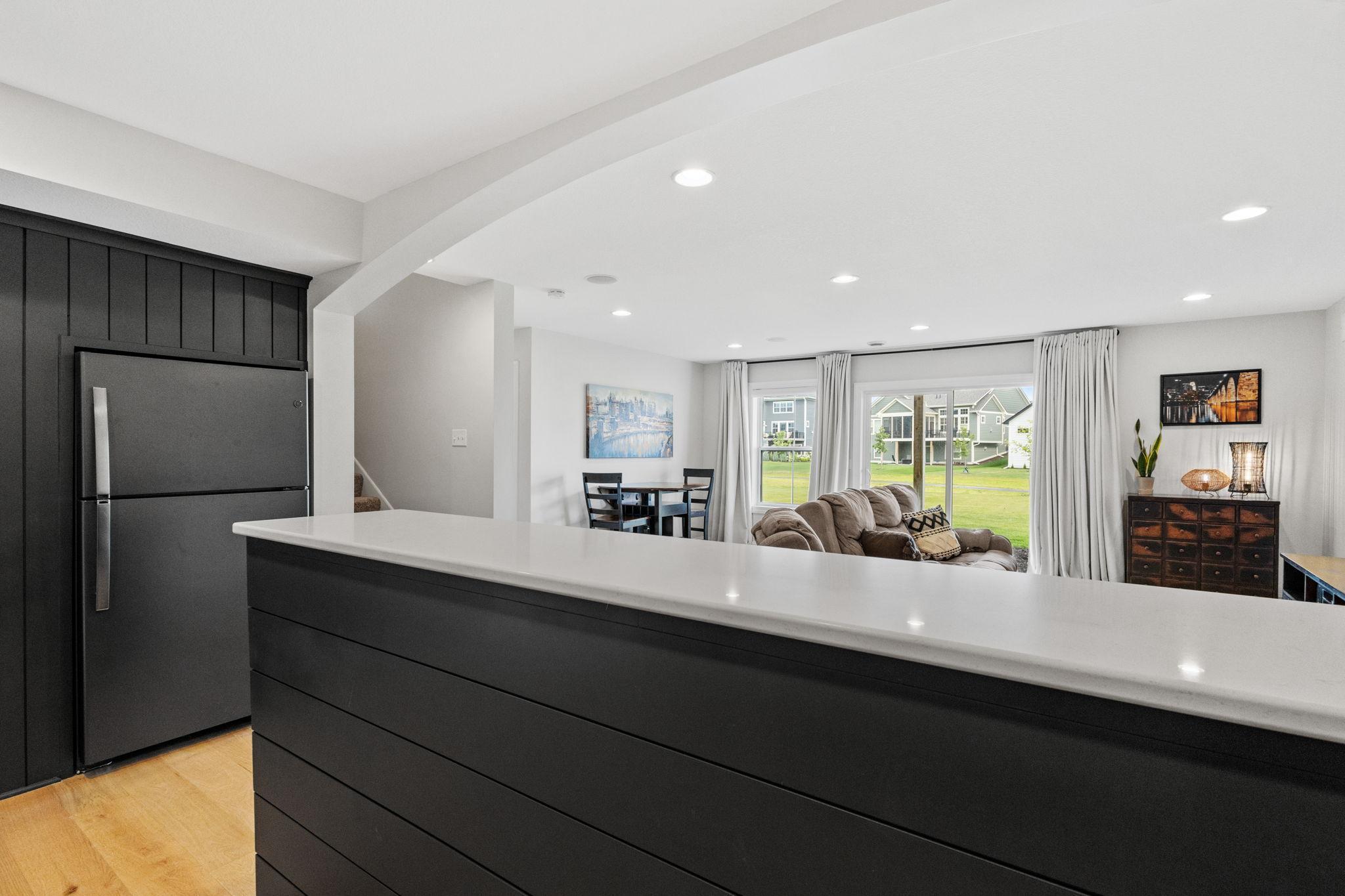 Kitchen island with dark cabinetry overlooks a furnished living area and sliding glass doors.
