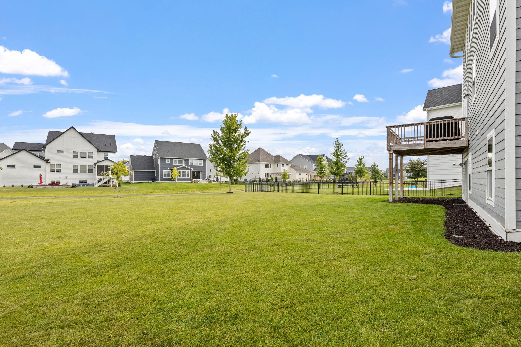 Broad backyard lawn beside a gray house with a raised wooden deck and fenced neighboring yards.